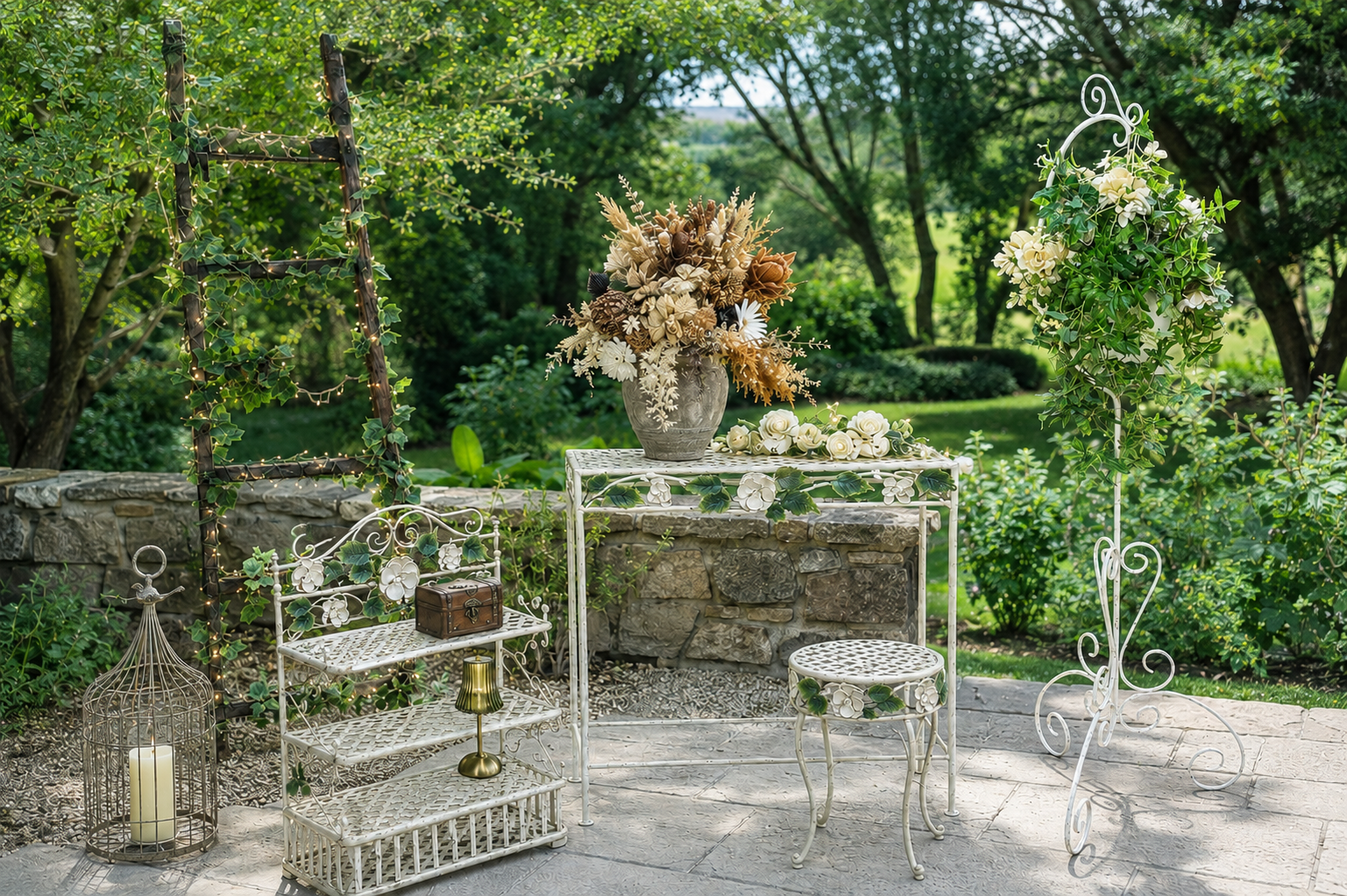 Decorative outdoor garden setting with white metal furniture, a birdcage with a candle, a small table with a floral arrangement, and lush greenery in the background.