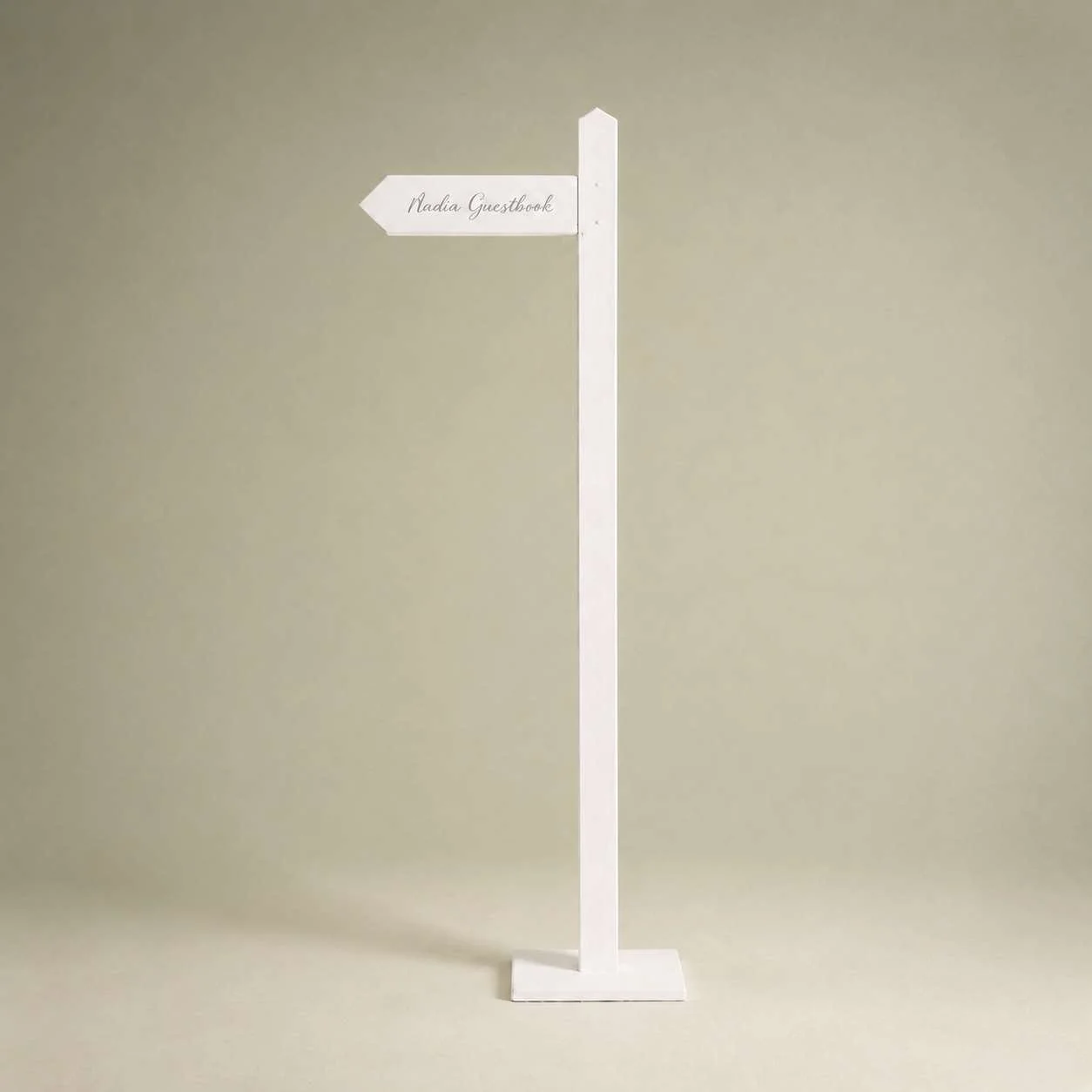 White signpost with an arrow pointing left that says 'Nadia Guestbook' on a plain beige background.