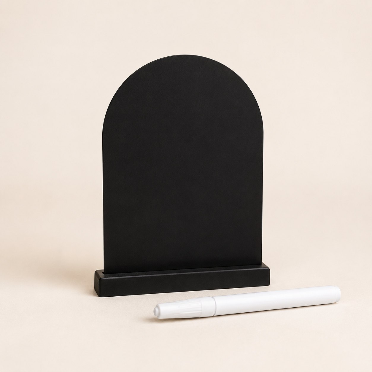 A black arch-shaped chalkboard with a white chalk marker lying in front, on a beige background.