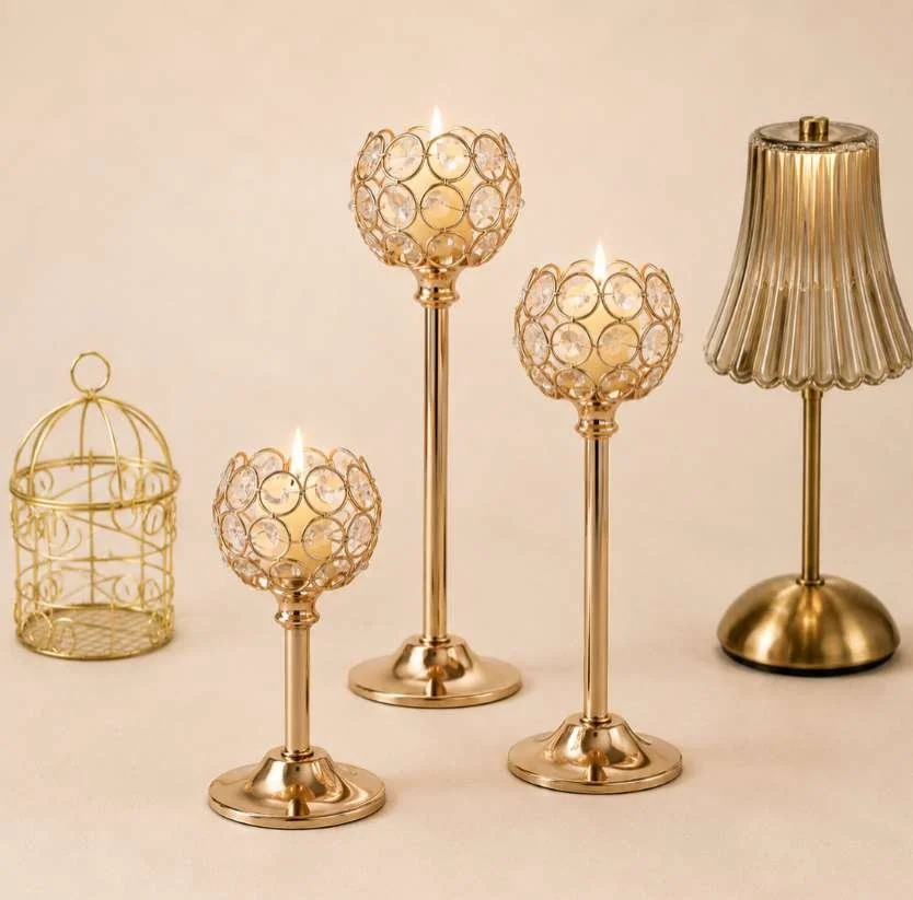 Gold decorative candles and a gold table lamp on a beige surface.