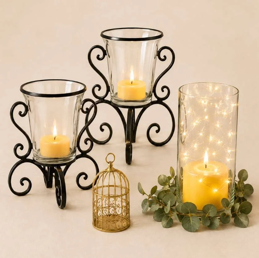 Decorative candles with black metal holders, a small gold birdcage, and eucalyptus leaves on a beige surface.