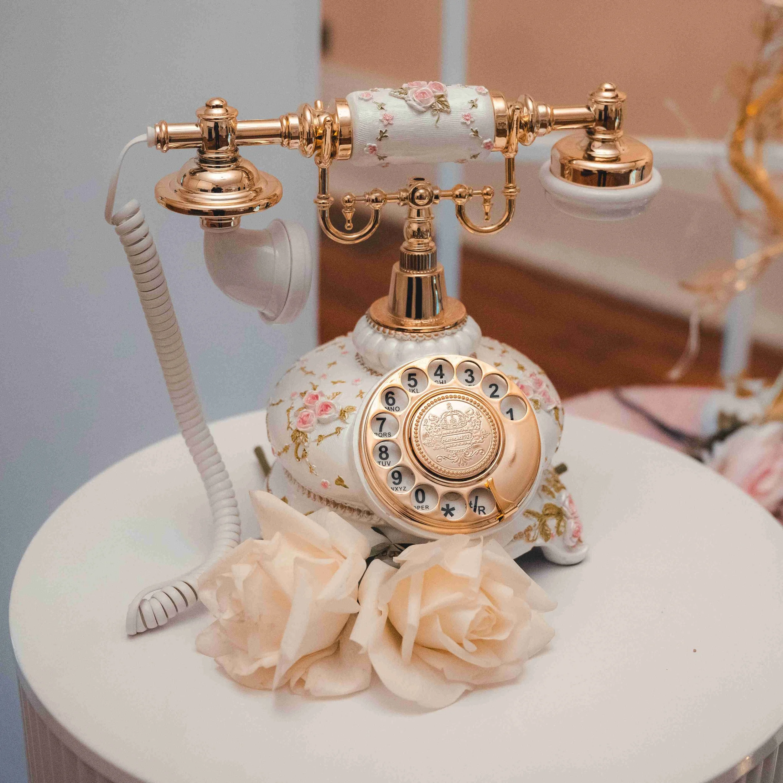 Cream-colored, floral-embellished vintage rotary telephone on a white table.