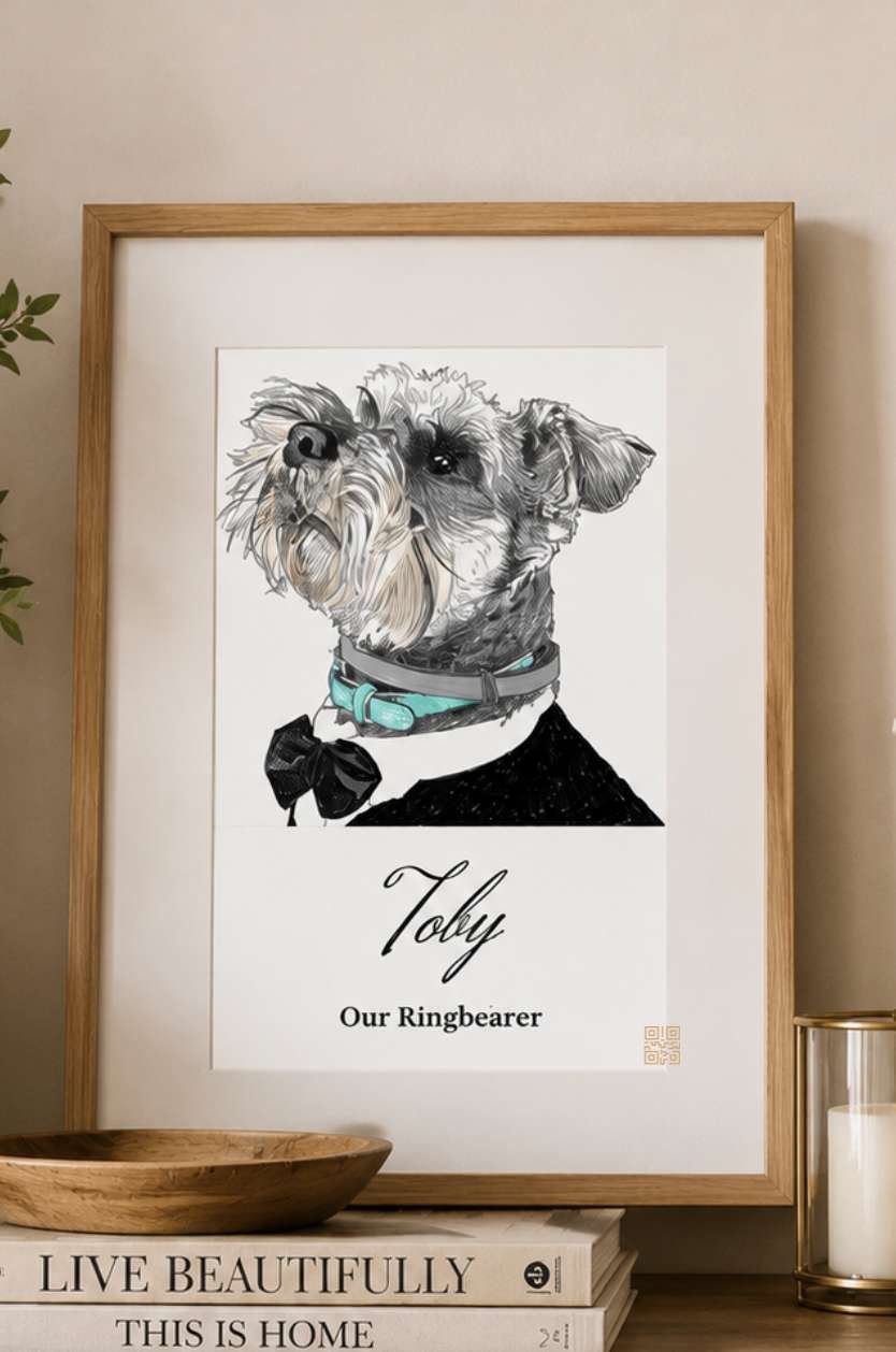 A framed black and white illustration of a dog named Toby, wearing a collar and a bow tie, with text below reading 'Toby Our Ringbearer.' The frame is on a surface with stacked books, a wooden bowl, and a candle in a glass holder nearby.