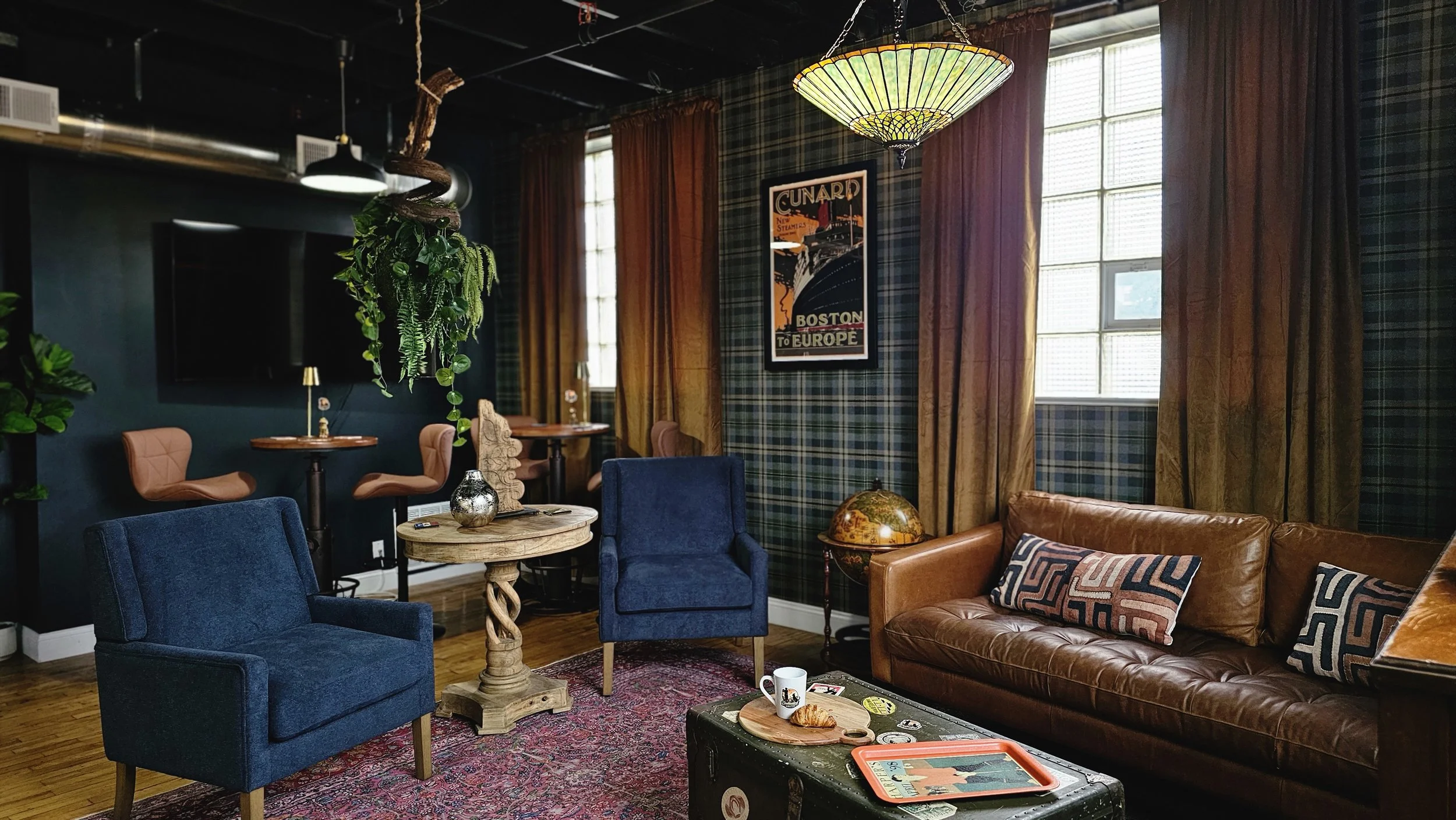 Cozy living room with colorful plaid and solid curtains, blue and brown sofas, a wooden coffee table, plants, vintage decor, and framed art on the walls.