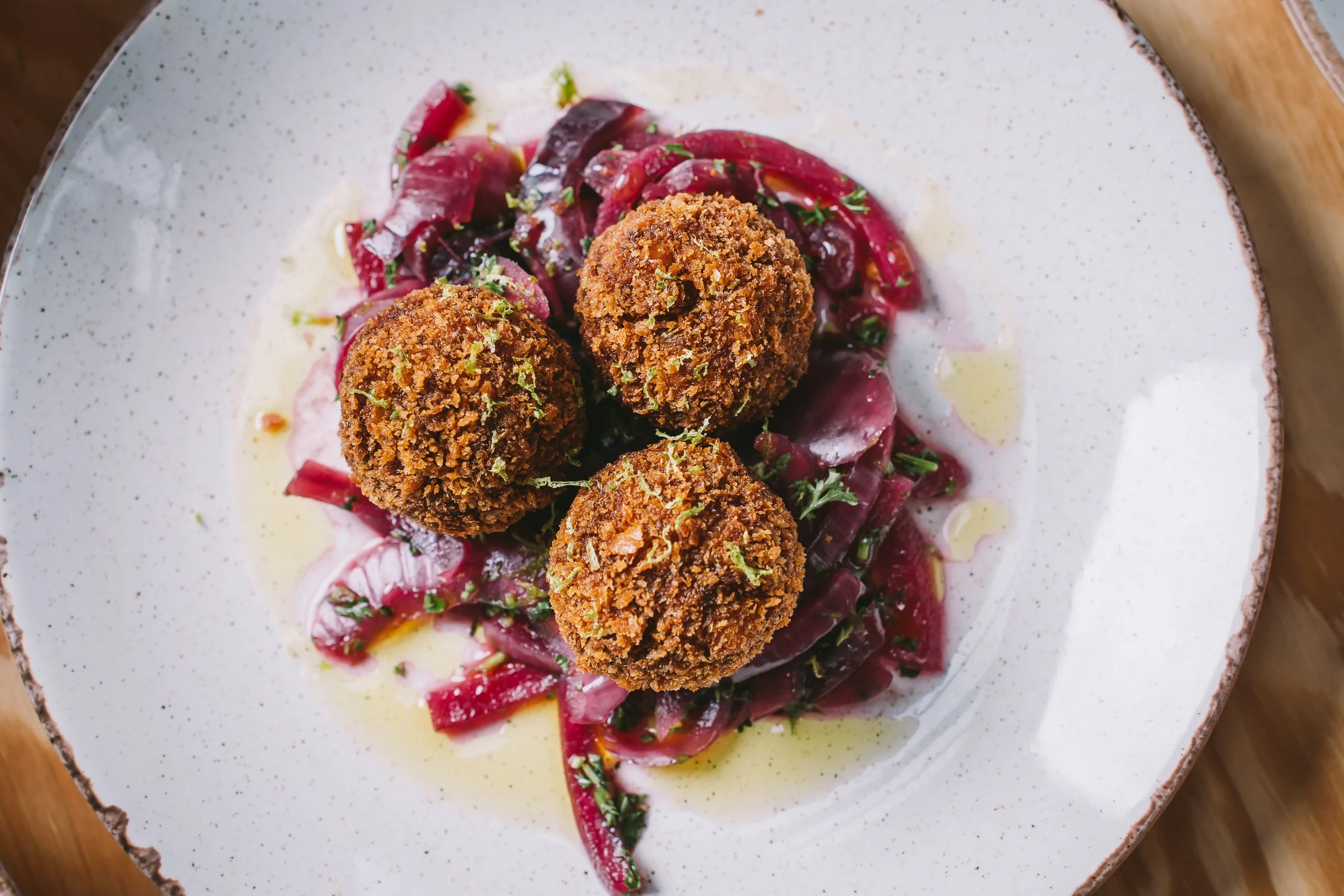 Plate of breaded fried croquettes on a bed of beetroot salad with herbs and dressing.