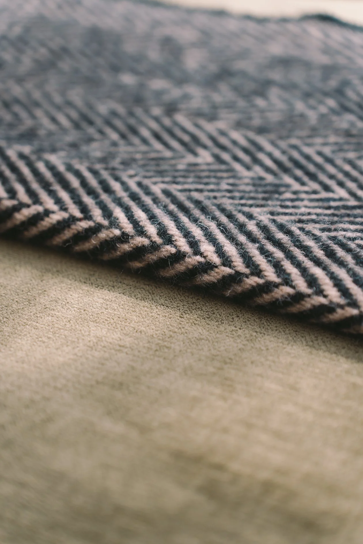 Close-up of a textured knitted fabric with black and beige stripes, resting on a soft beige surface.
