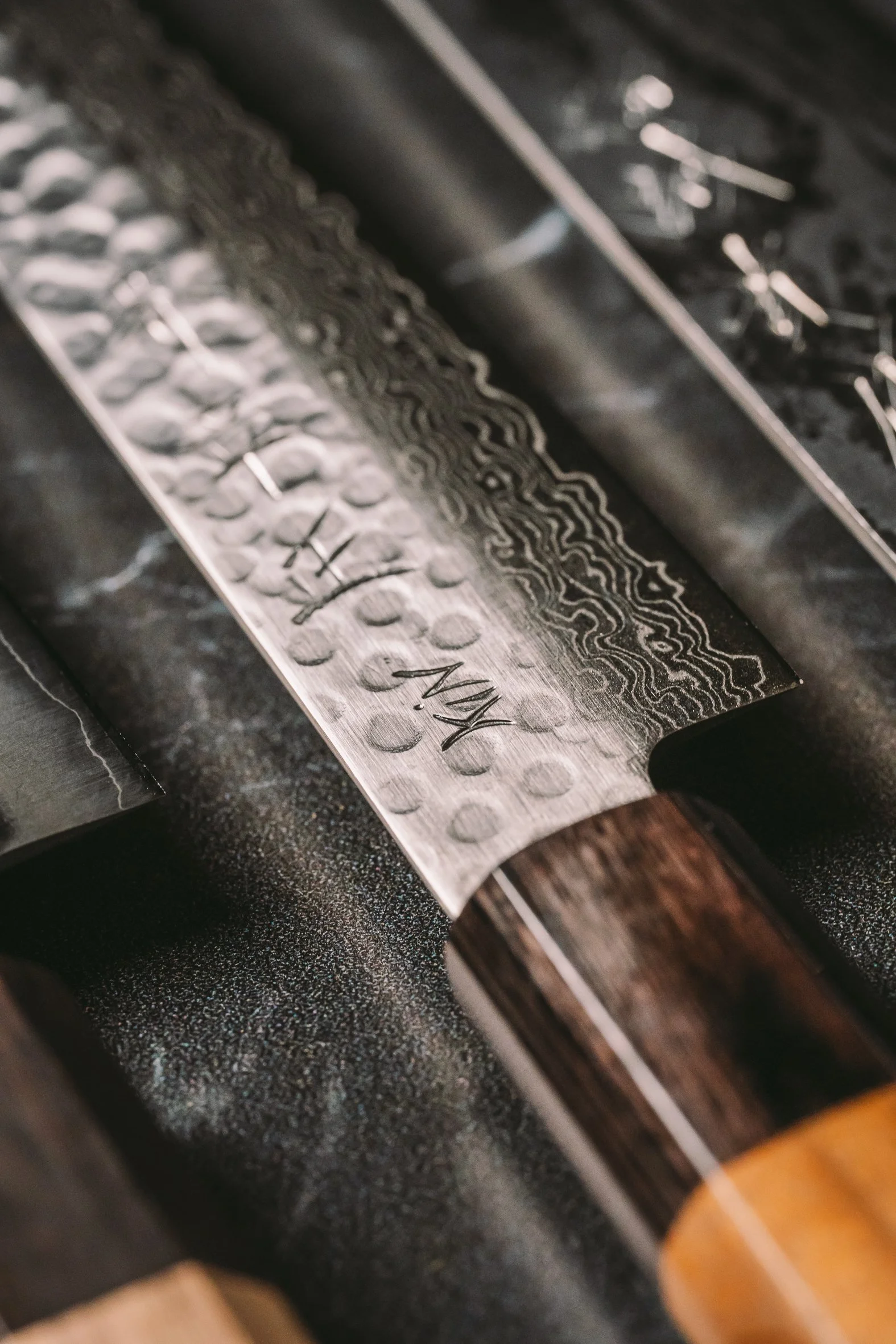 Close-up of a textured metal knife blade with etched markings, mounted on a dark surface.