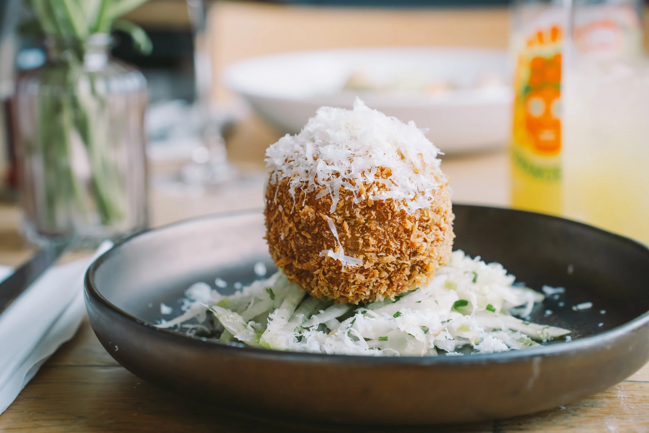 A breaded and fried food item topped with shredded cheese, served on a bed of shredded lettuce in a black bowl.