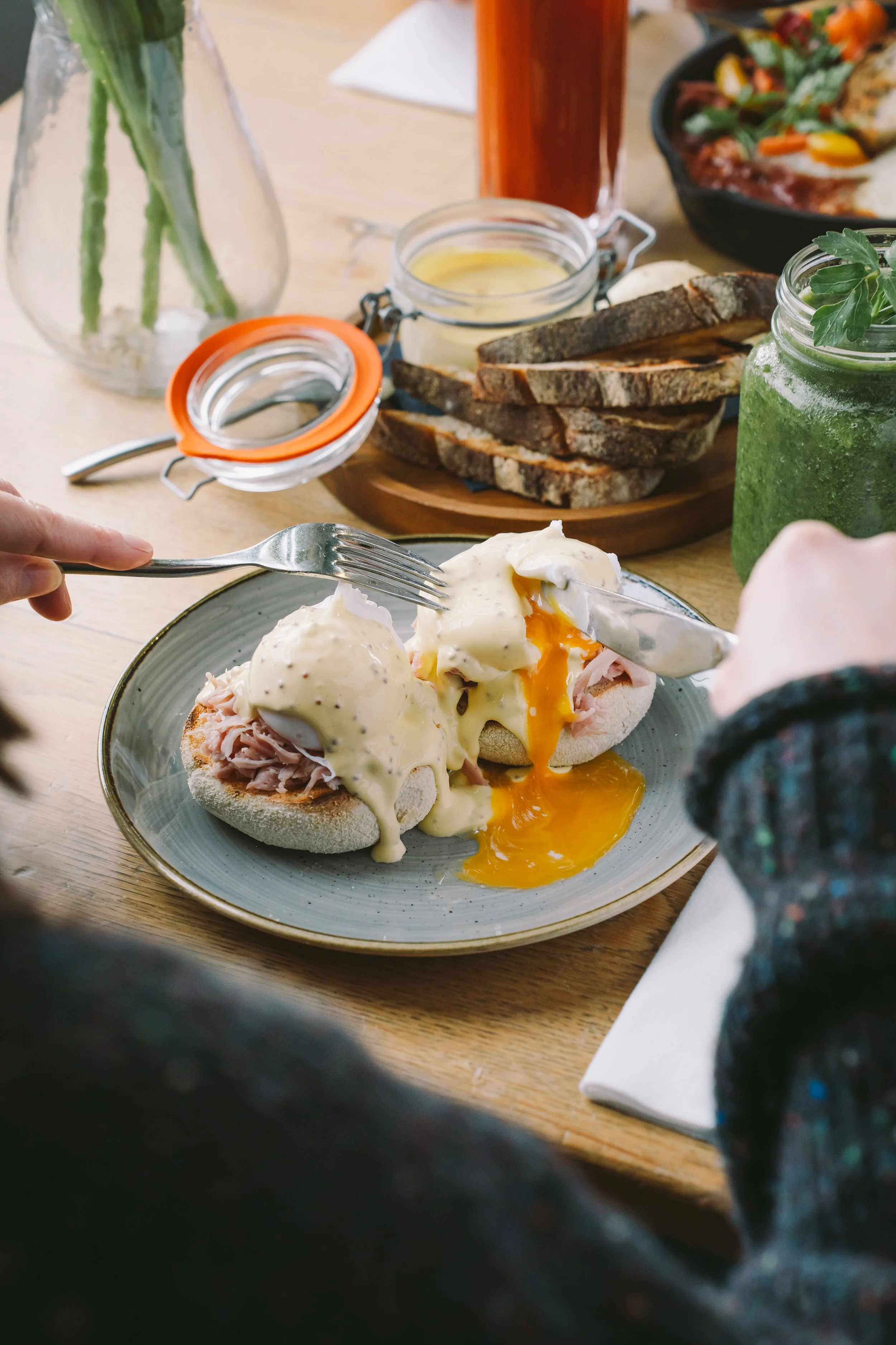A plate with eggs Benedict topped with hollandaise sauce, served with ham on an English muffin. The dish is on a gray plate on a wooden table.
