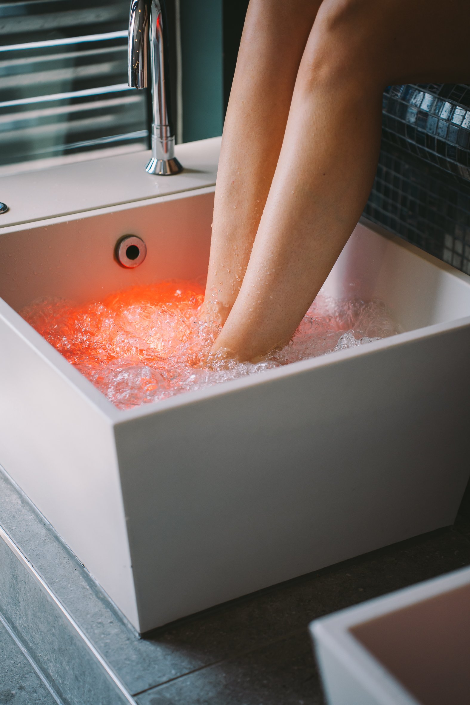 Person soaking their legs in a foot spa with red light therapy.