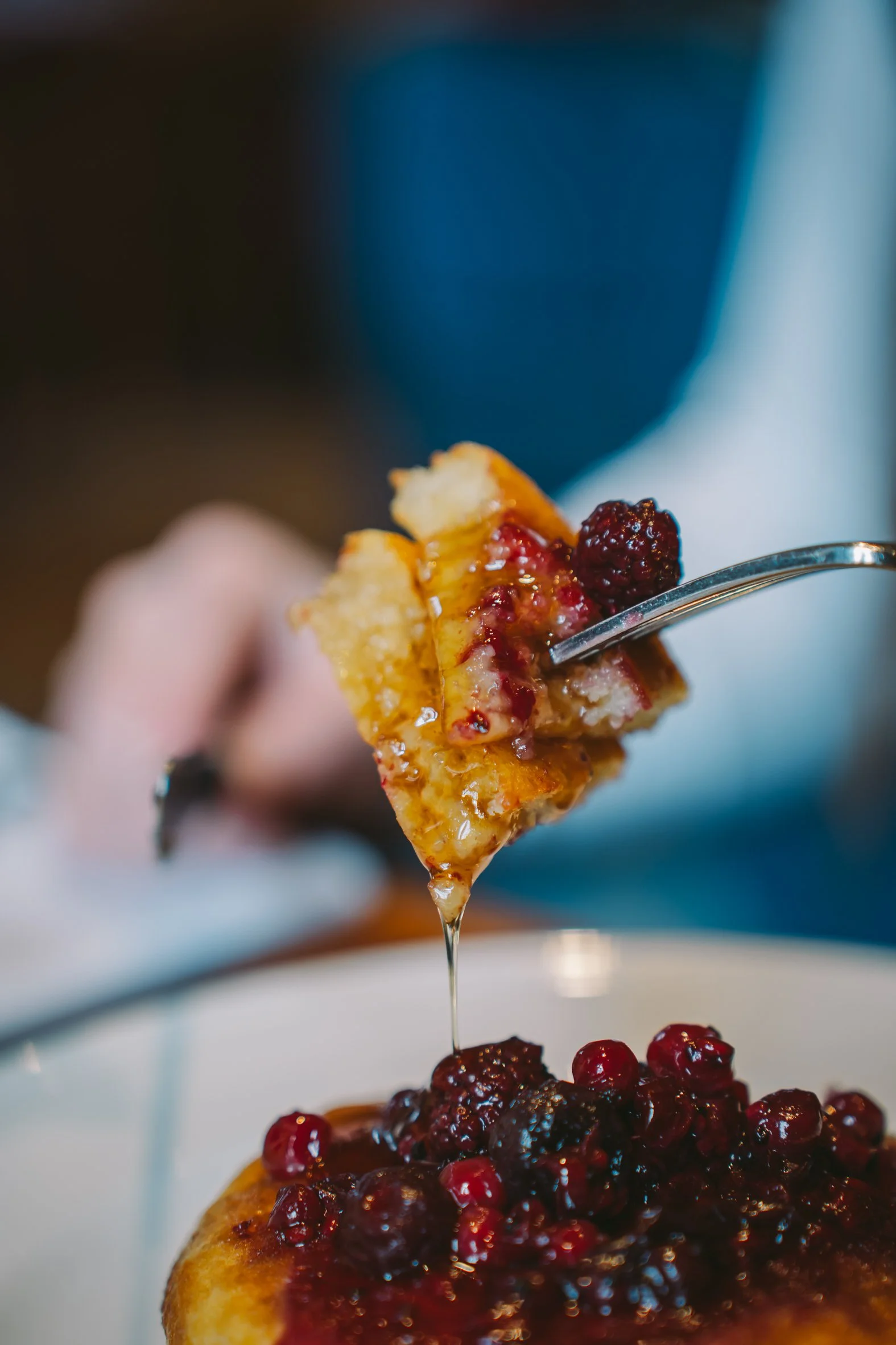 A slice of pie topped with mixed berries, with syrup dripping from a fork held above it.