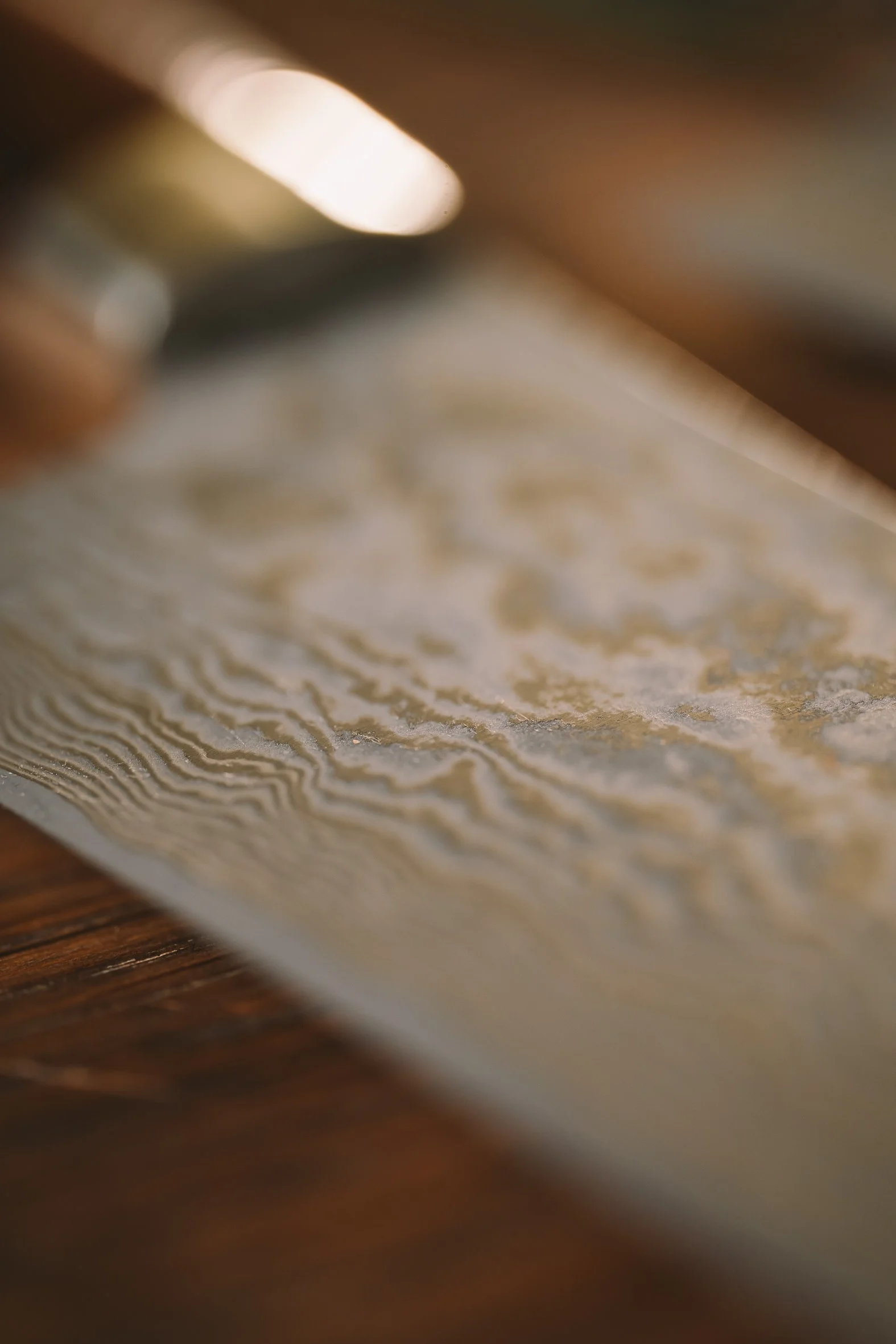 Close-up image of a textured beige surface with intricate wavy patterns, with blurred background indicating possibly a paper or fabric material.