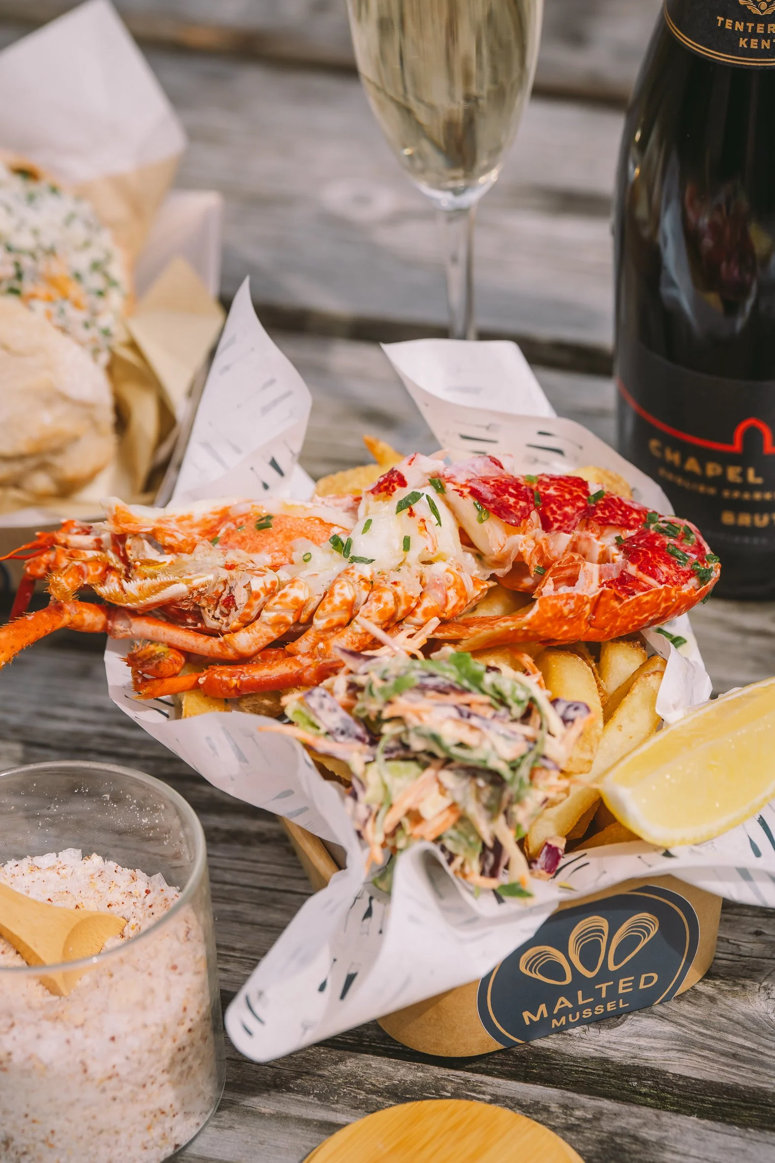 A tray of seafood fries with lobster and shrimp, garnished with green herbs, accompanied by lemon wedges and a bowl of seafood salt on a wooden table.