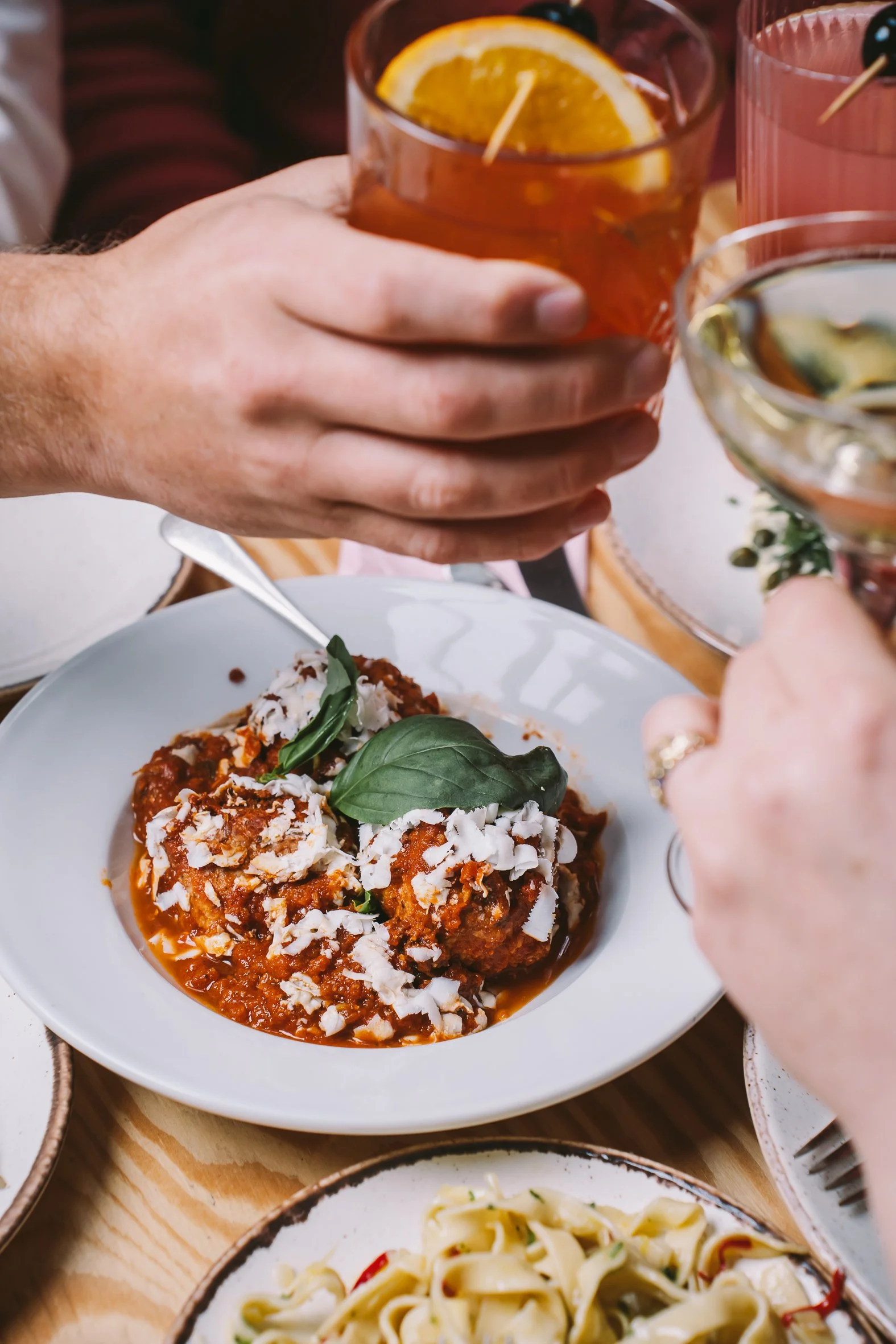 People sharing drinks at a meal, with a plate of spaghetti as the main dish visible in the foreground.