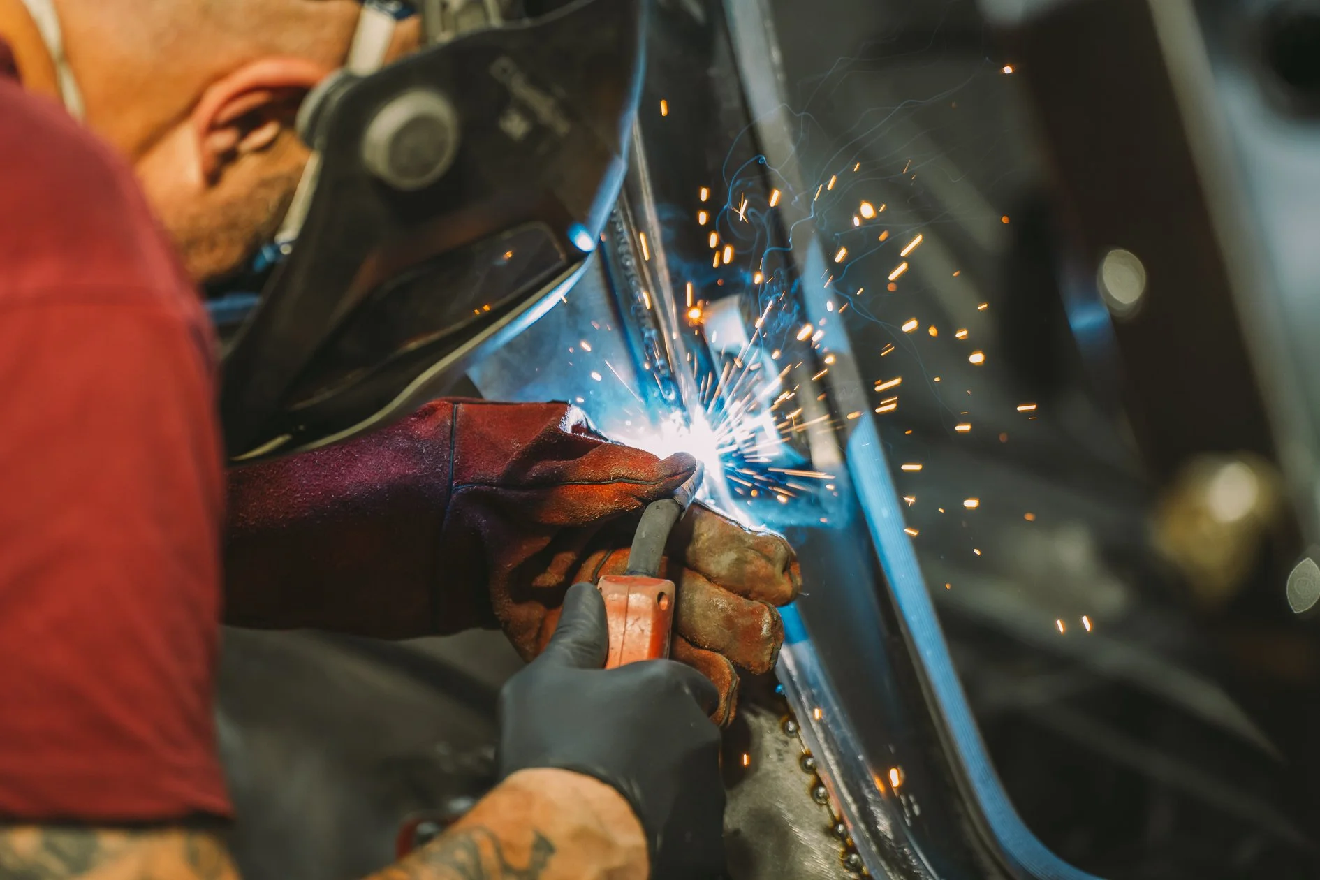 A person welding metal with a welding arc, sparks flying, wearing protective gloves and a welding helmet.