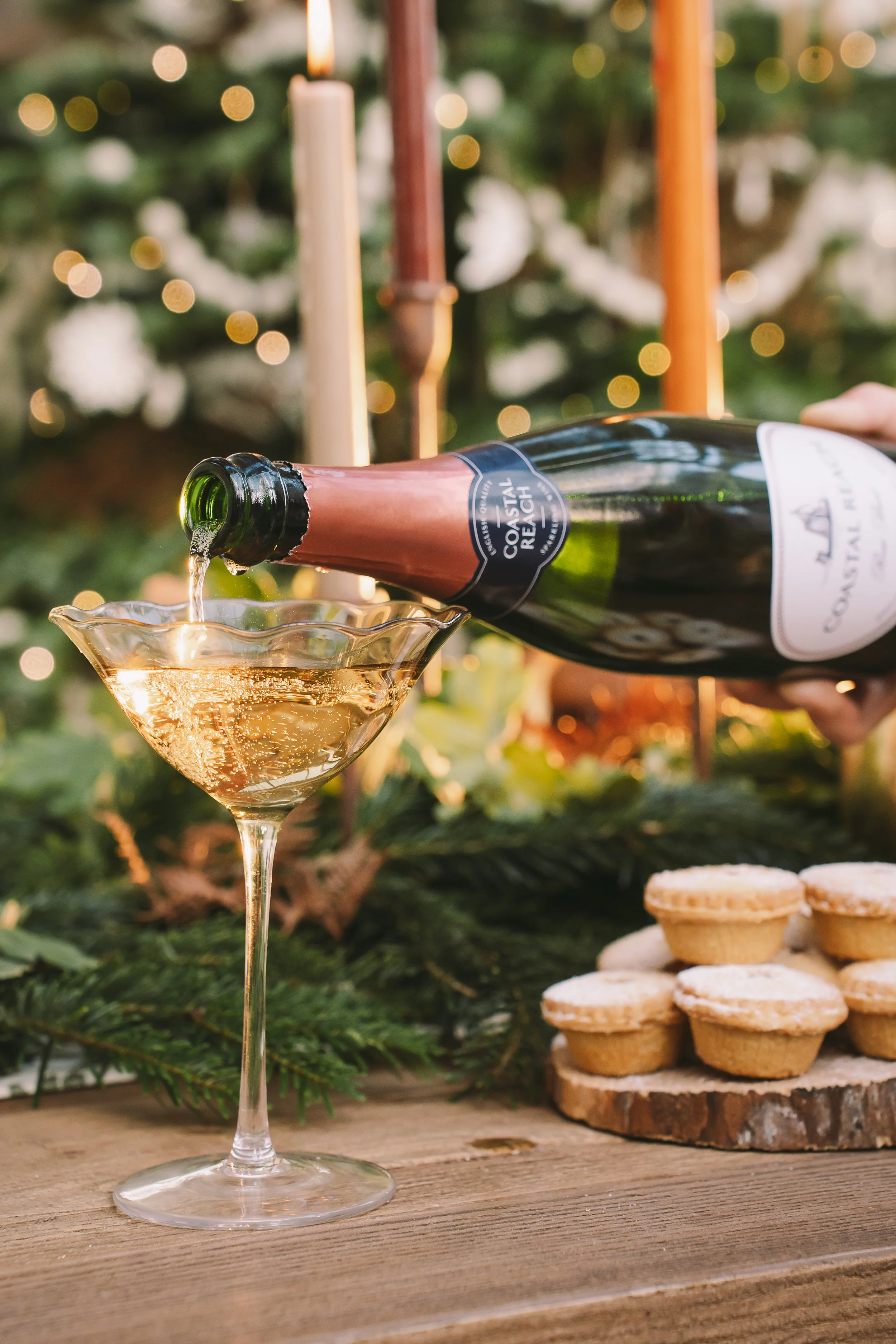 A bottle of sparkling wine being poured into a glass, with a background of Christmas decorations, cookies, and blurred lights.