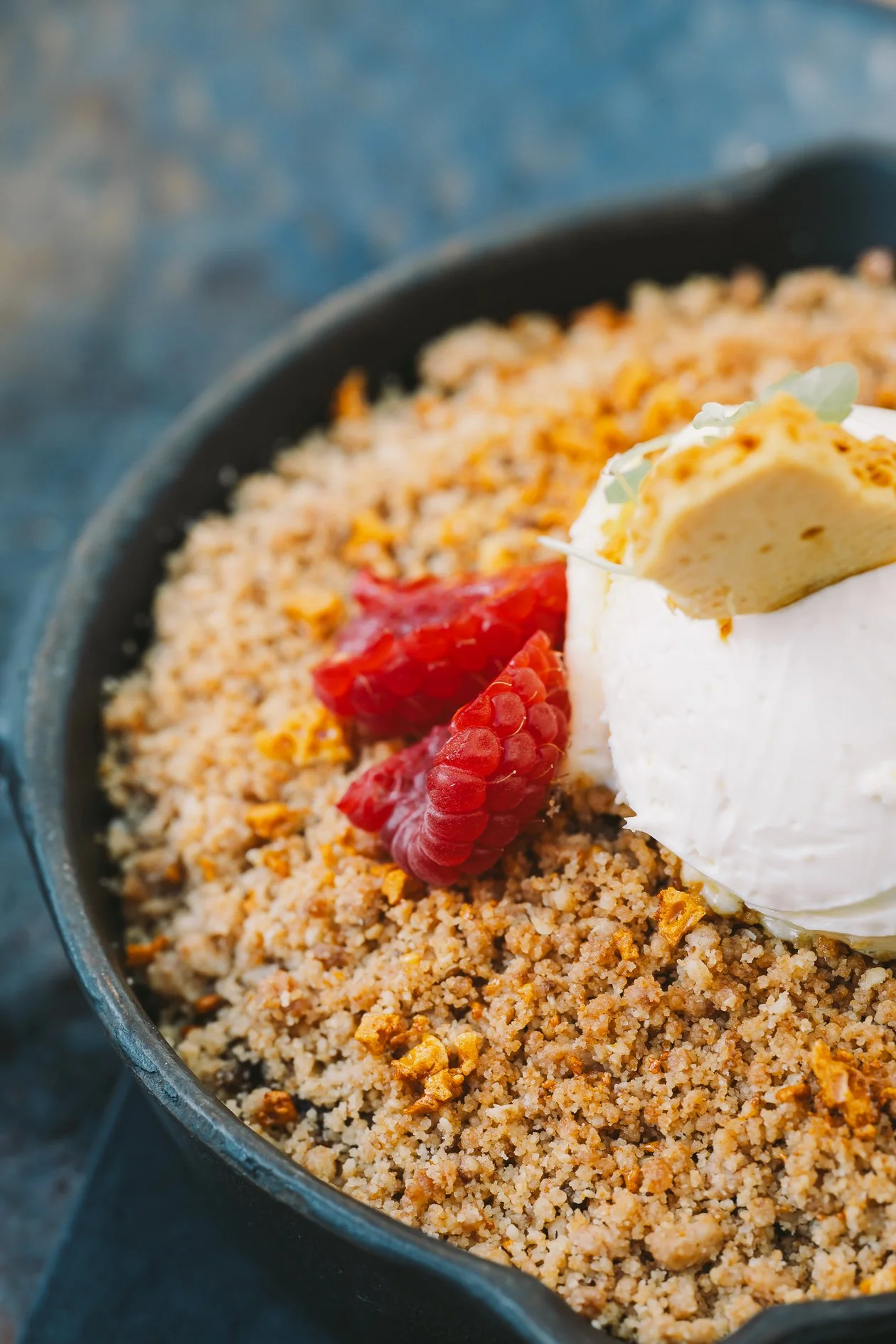 Baked crumble topped with whipped cream, garnished with raspberries and a piece of cookie or biscuit, in a baking dish.
