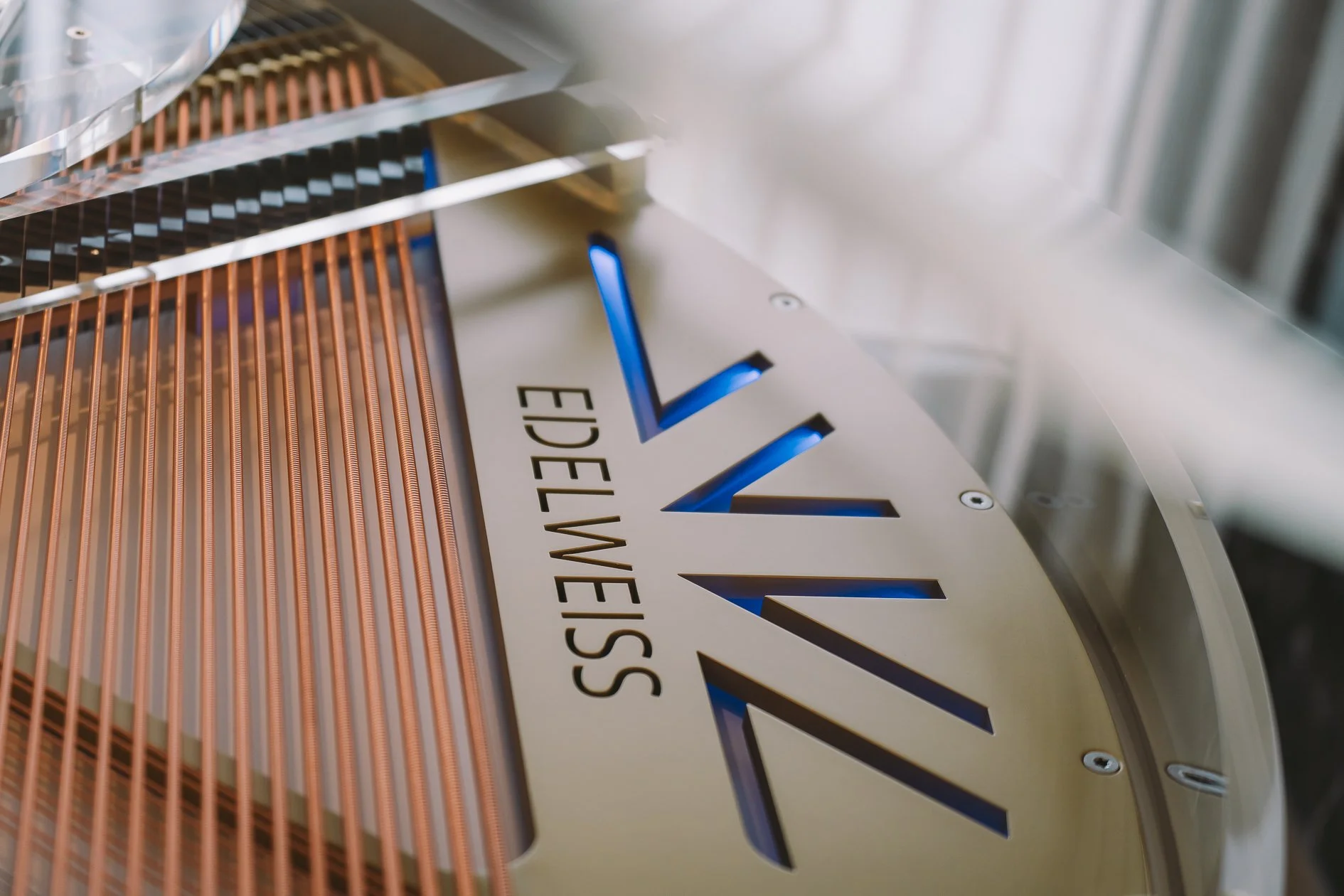 Close-up photo of a metallic sign with the word 'ATM' illuminated in blue and the phrase 'Edelweiss' partially visible below, with metallic and copper-colored elements around it.