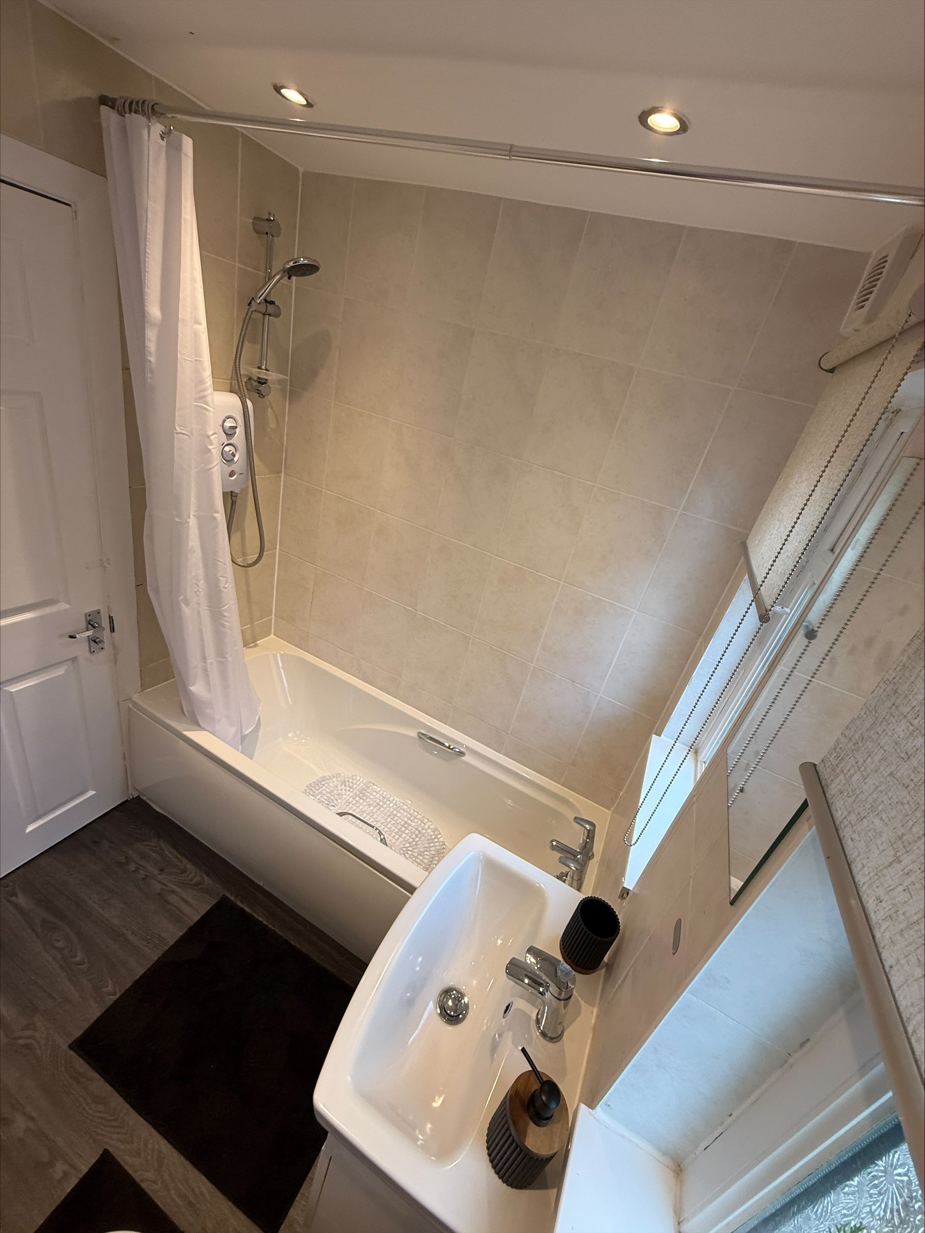 Bright bathroom with a bathtub, shower, white curtain, tiled walls, sink vanity, and window blinds