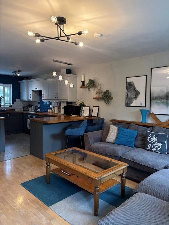 Modern open-concept living room and kitchen with blue cabinets, gray sectional sofa, wood coffee table, and contemporary lighting