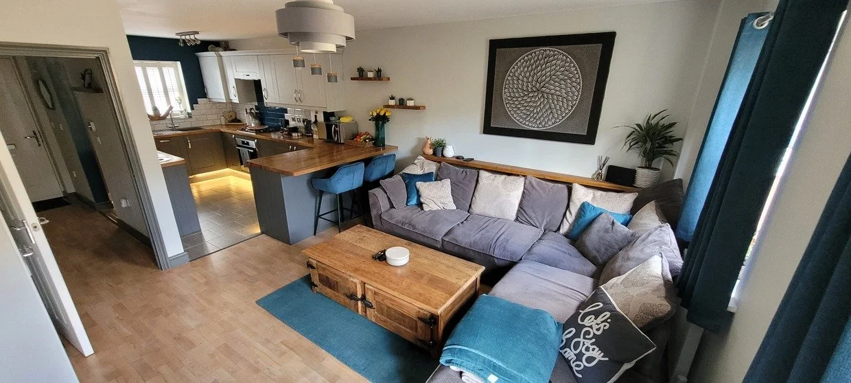 Open-plan living room with gray sectional sofa, wooden coffee table, blue rug, and modern kitchen with island and bar stools