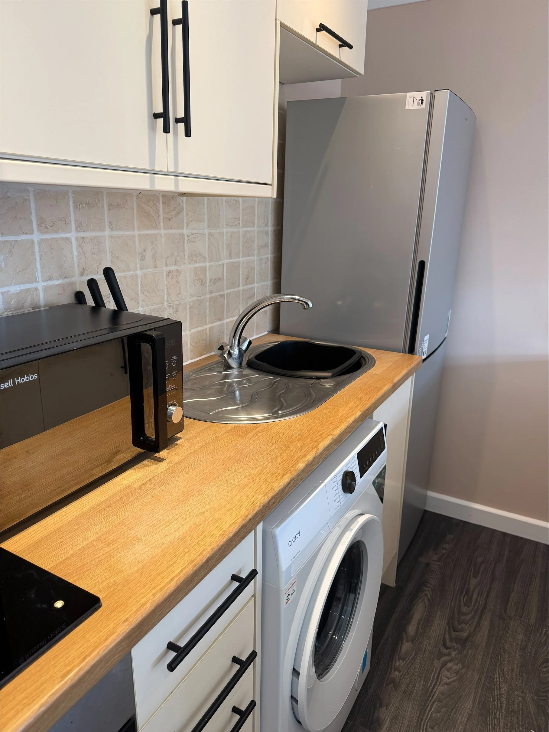 Compact modern kitchen with white cabinets, wood countertop, microwave, sink, refrigerator, and front-loading washing machine