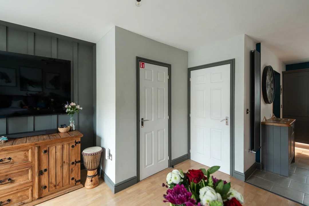 Modern living room with wall-mounted TV, wooden cabinet, floral arrangement, and two white interior doors
