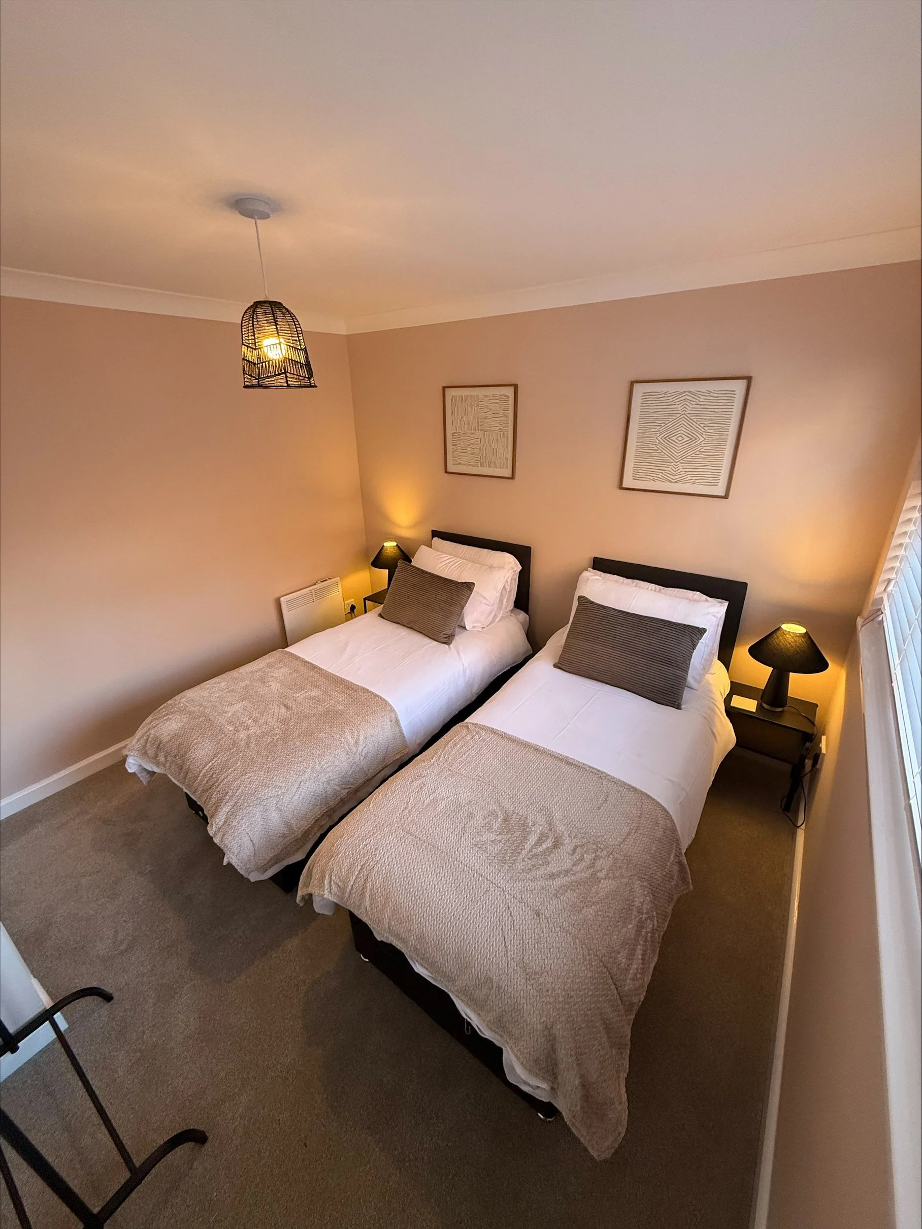 Cozy twin bedroom with two neatly made beds, bedside lamps, wall art, and a hanging pendant light.