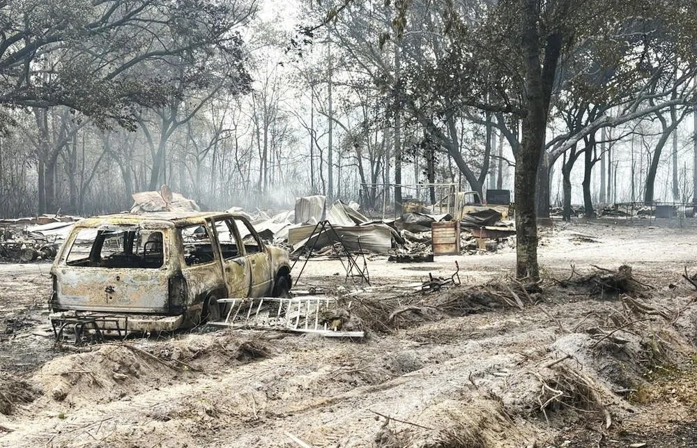 Cars, a trailer home and trees are burned into shades of skeletal gray after the Highway 82 fire in Brantley County, Ga., on April 22, 2026.