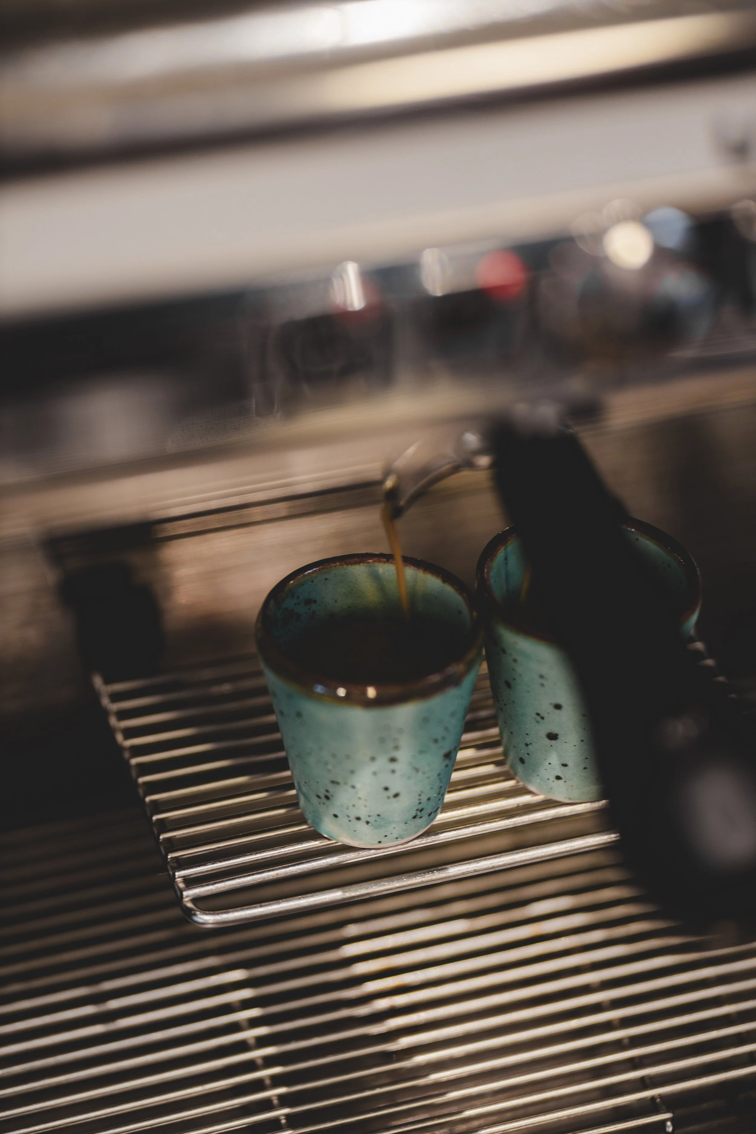 Två koppar med kaffe på en trådkorg under en espressomaskin.