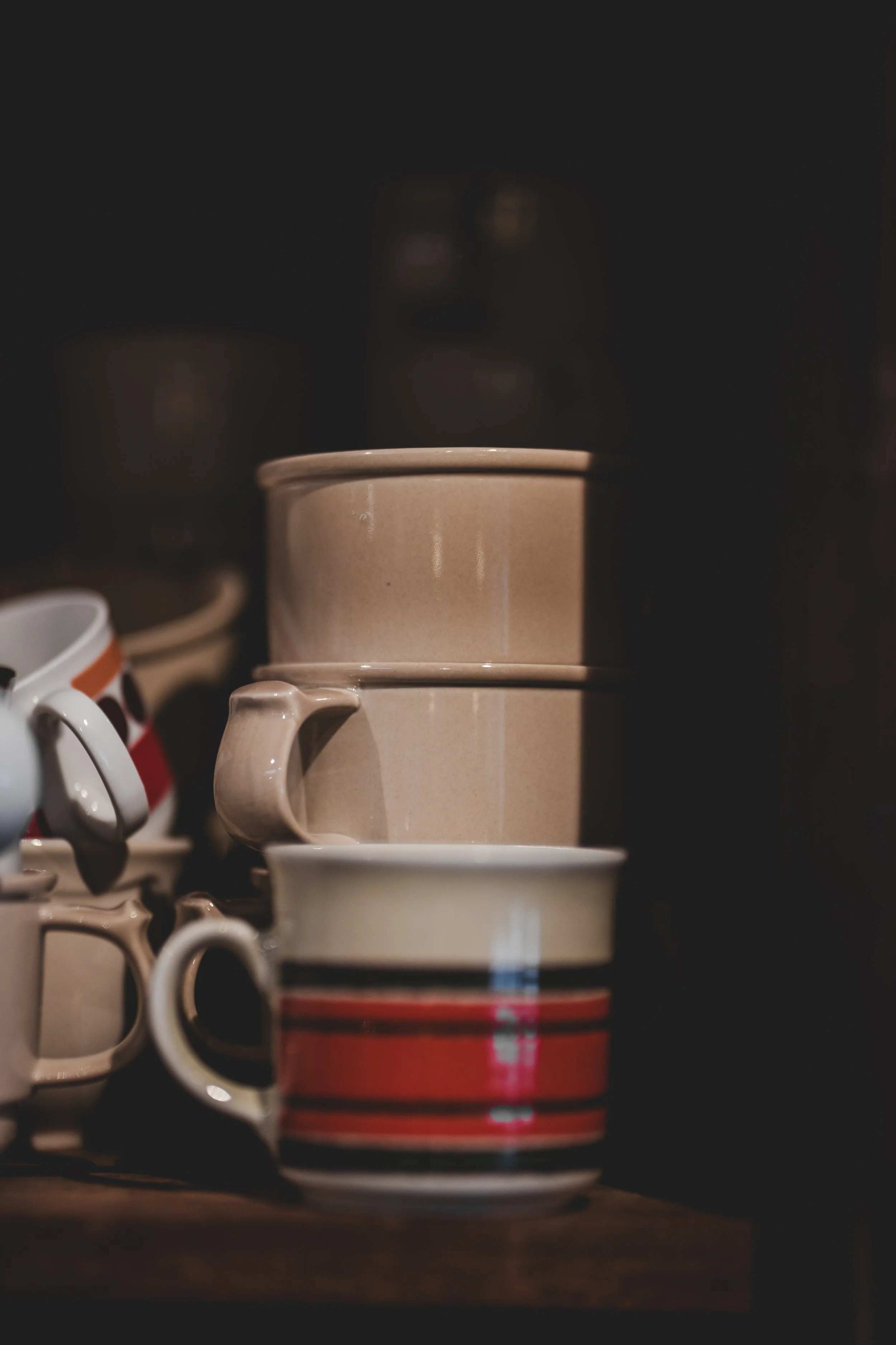 Flera kaffemuggar staplade på varandra på en mörk bakgrund.