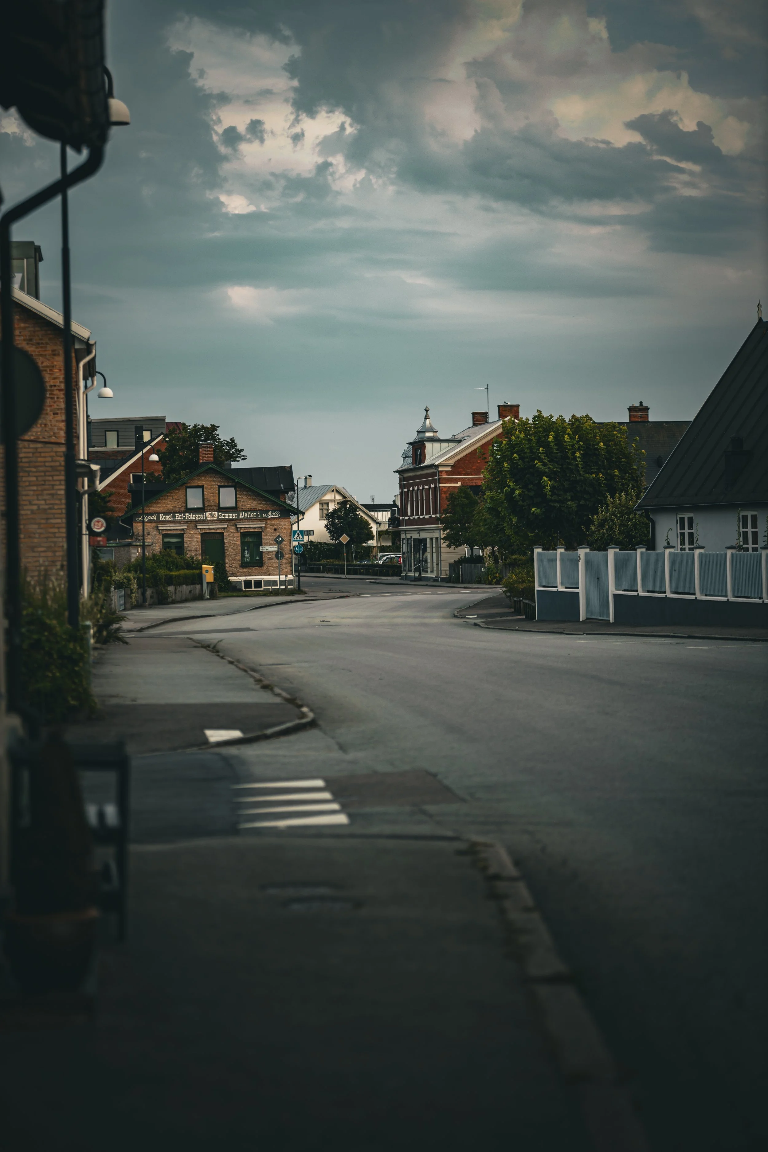 En tom stadsdel med ett överhängande mörkt molntäcke över ett fåtal byggnader i bakgrunden och en tom gata i förgrunden.