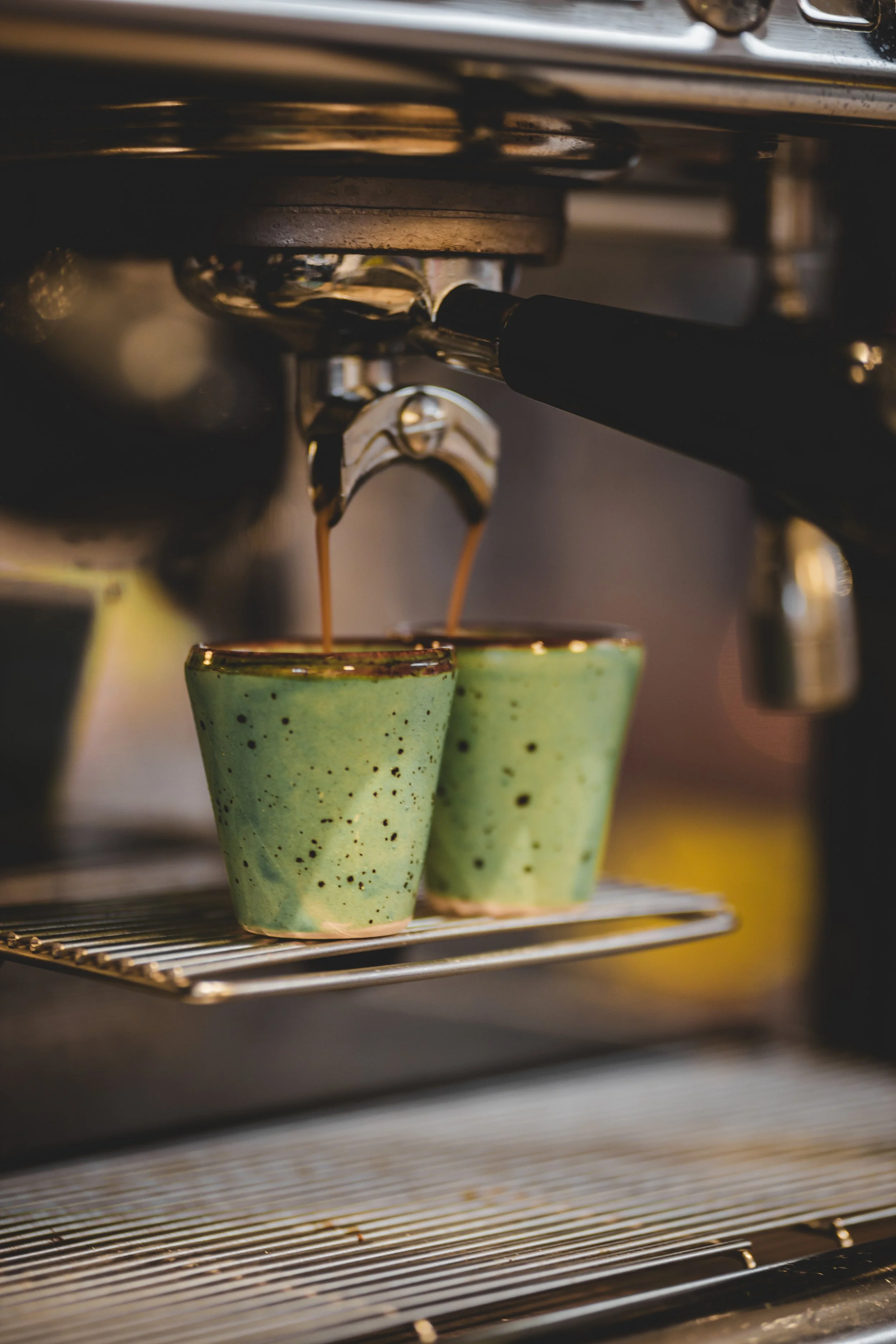 En espressomaskin som droppar varm espresso i gröna keramiska koppar.