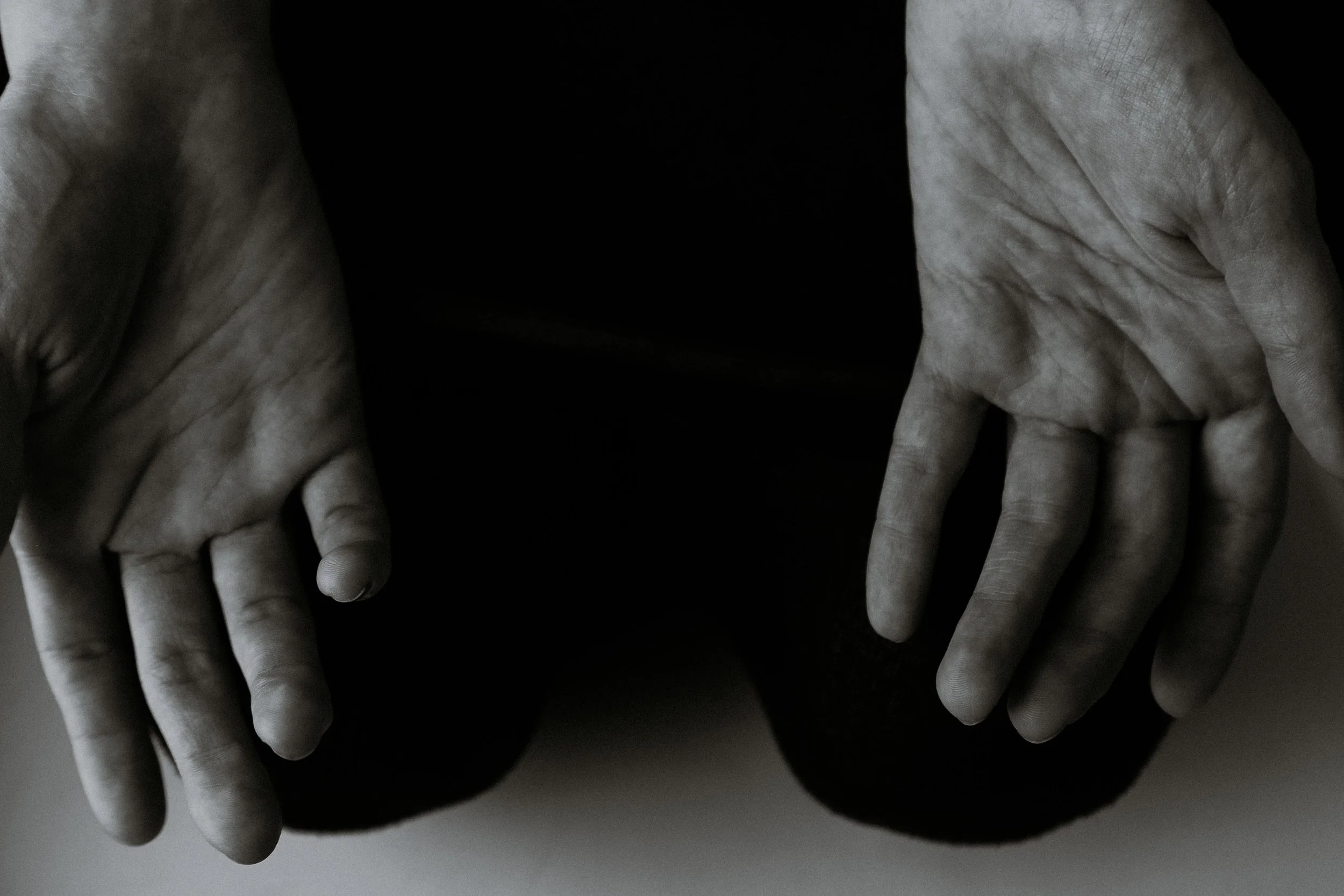 Close-up of two hands with interlocked fingers, appearing in grayscale with a stark black background.