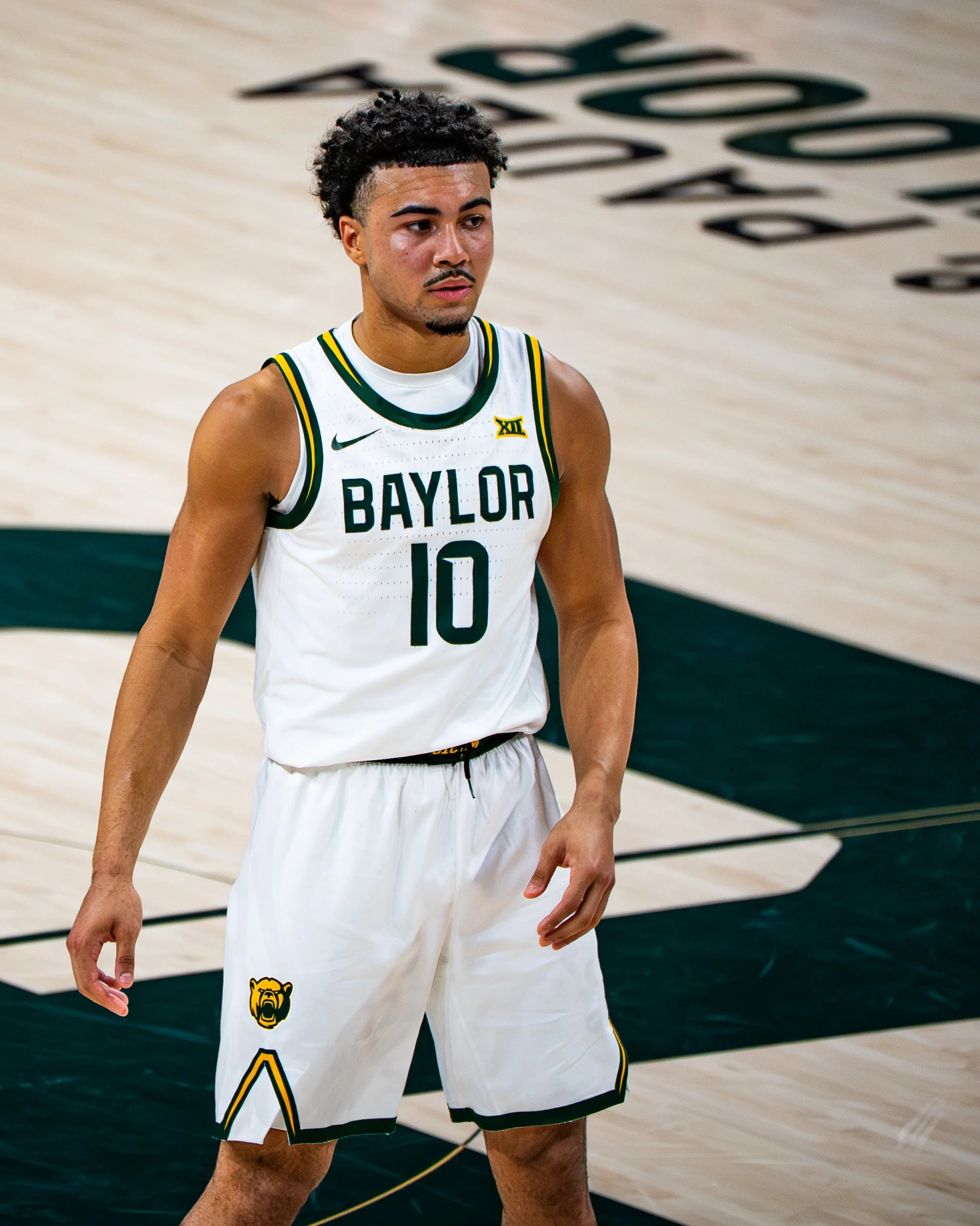 Close-up of a basketball player wearing a white Baylor University jersey with the number 10, standing on a basketball court.