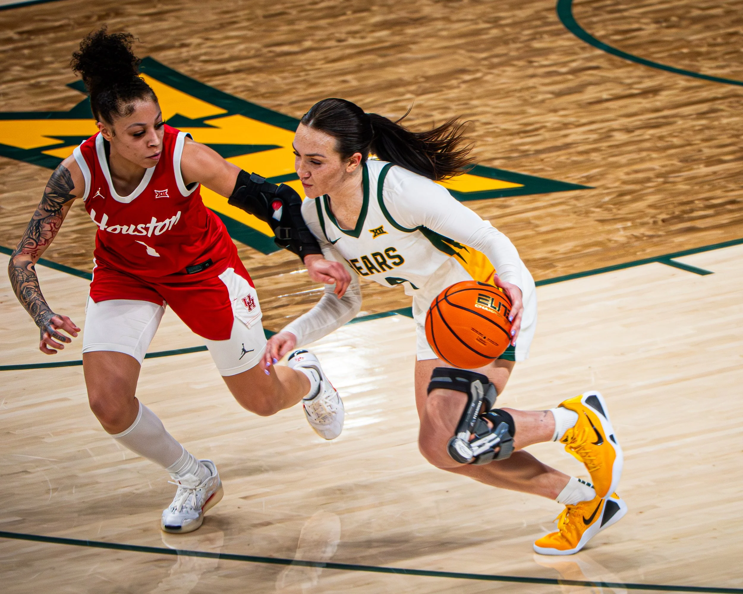 Two female basketball players from opposing teams compete for possession of the ball on a basketball court during a game.