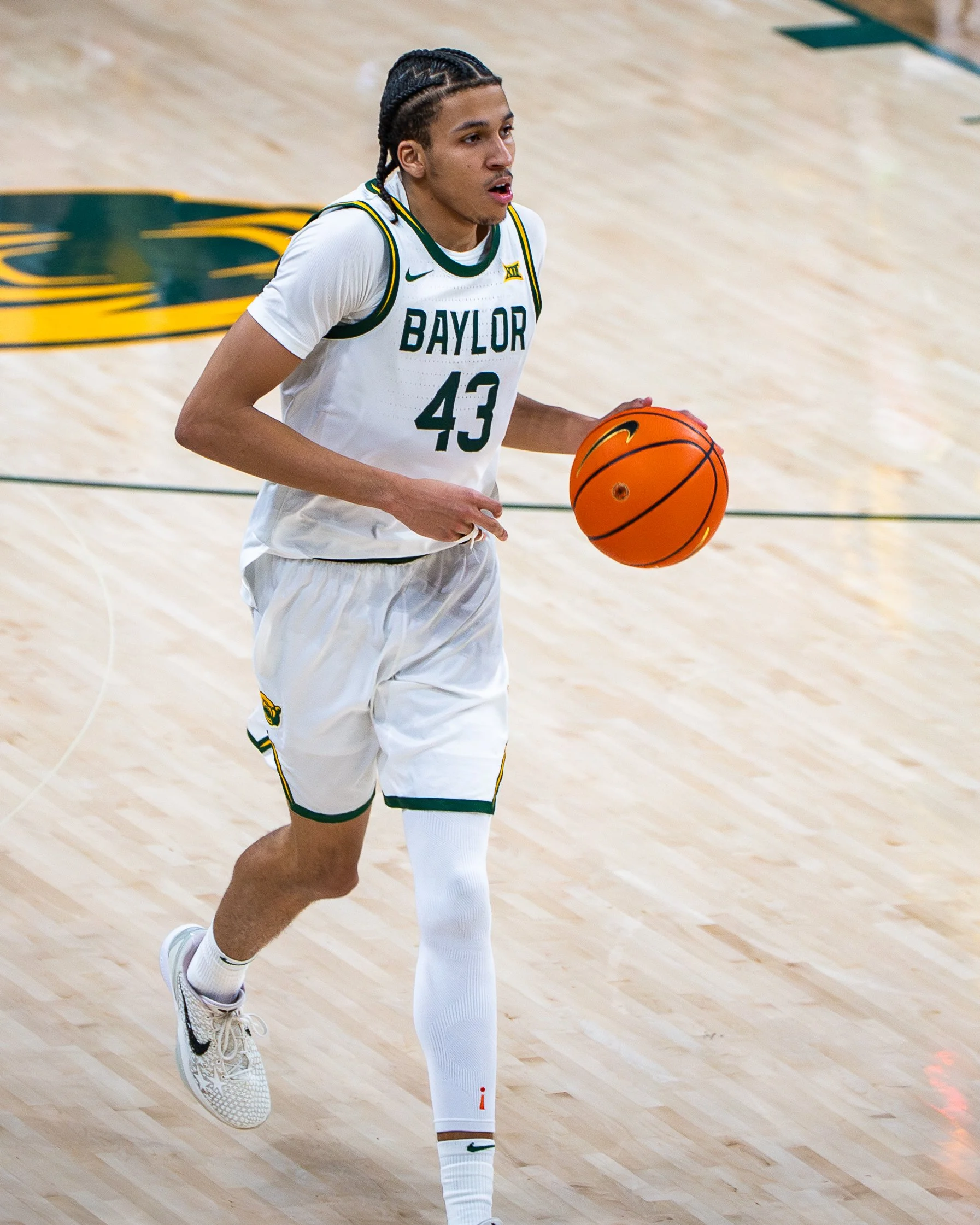 A basketball player in a white Baylor jersey with number 43 dribbling a basketball on the court.