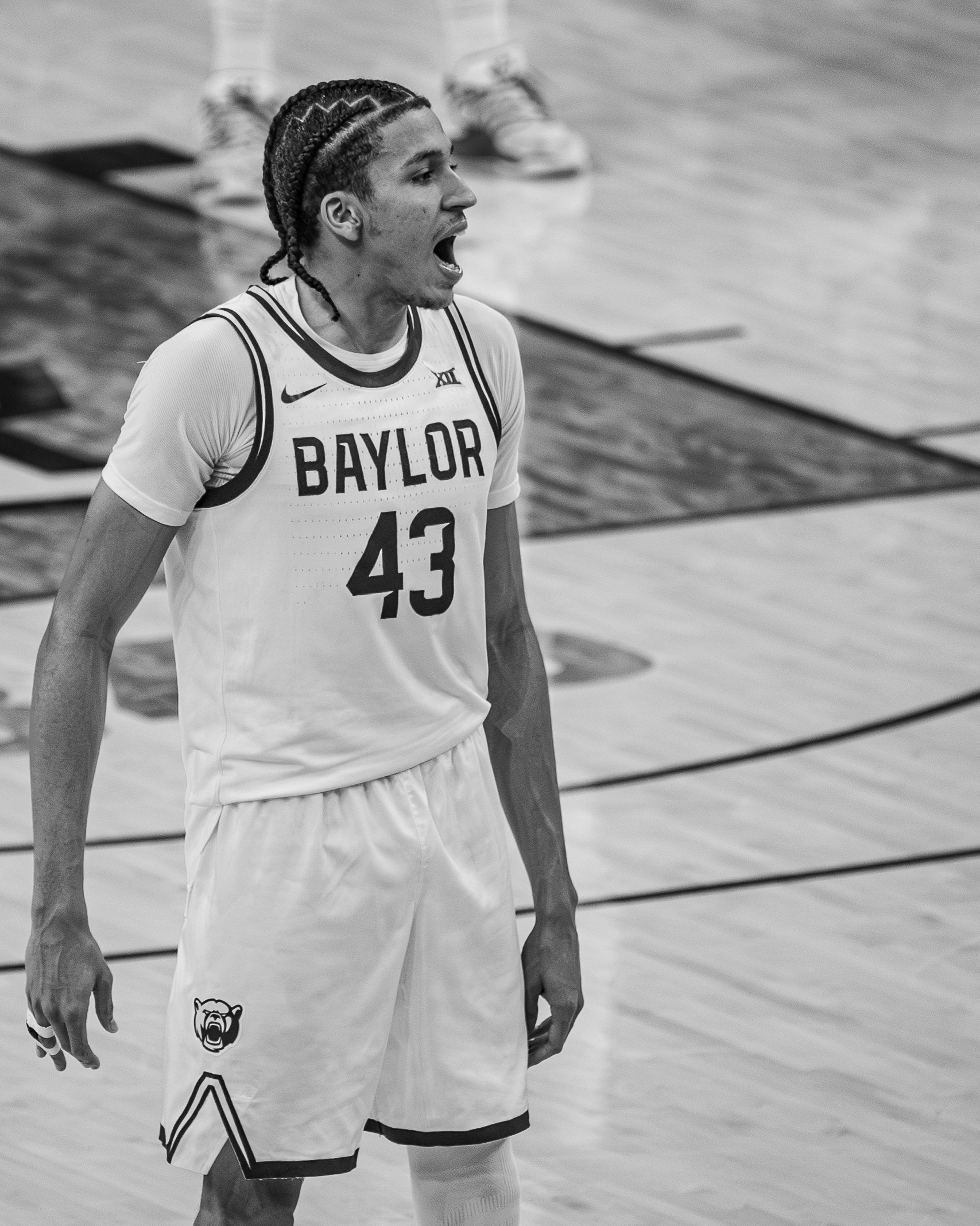A young male athlete with braided hair, wearing a white basketball uniform with 'Baylor' and the number 43, appears to be shouting or calling out during a game on a basketball court.