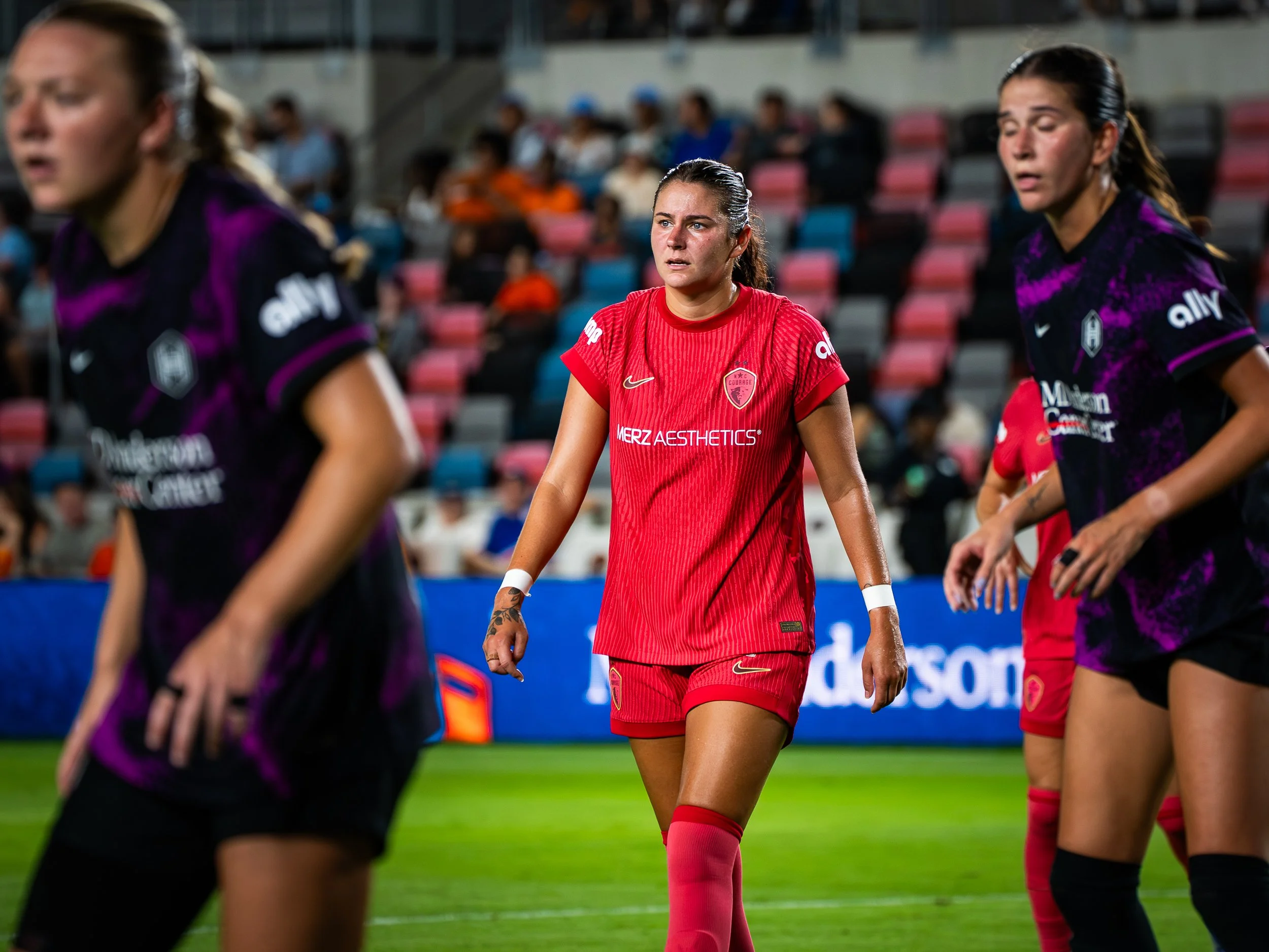 Female soccer players walking on the field during a game, focusing on one player in a red jersey.