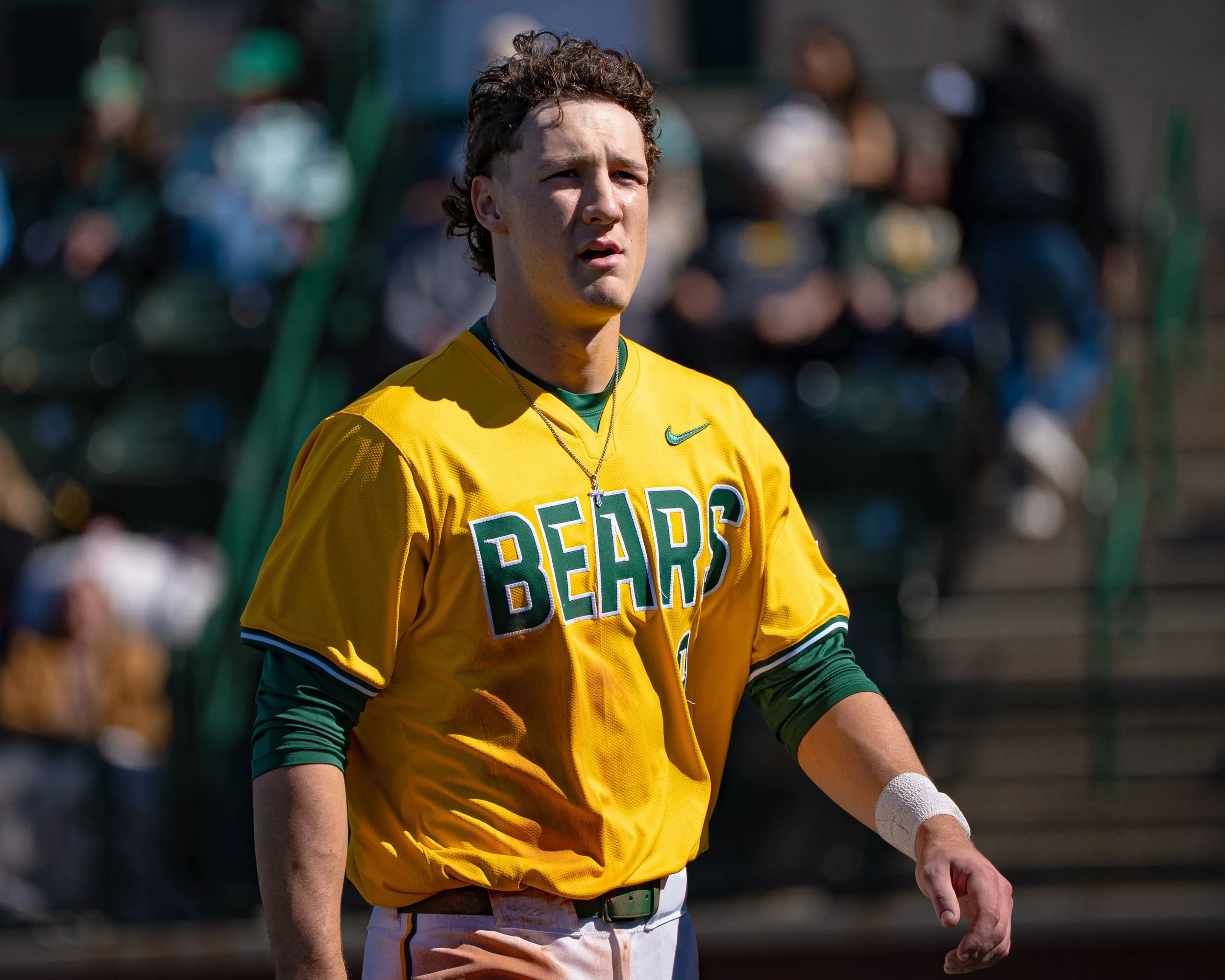 A young man in a yellow sports jersey with the word 'BEARS' on it stands outdoors with a concerned or focused expression, surrounded by blurred spectators.