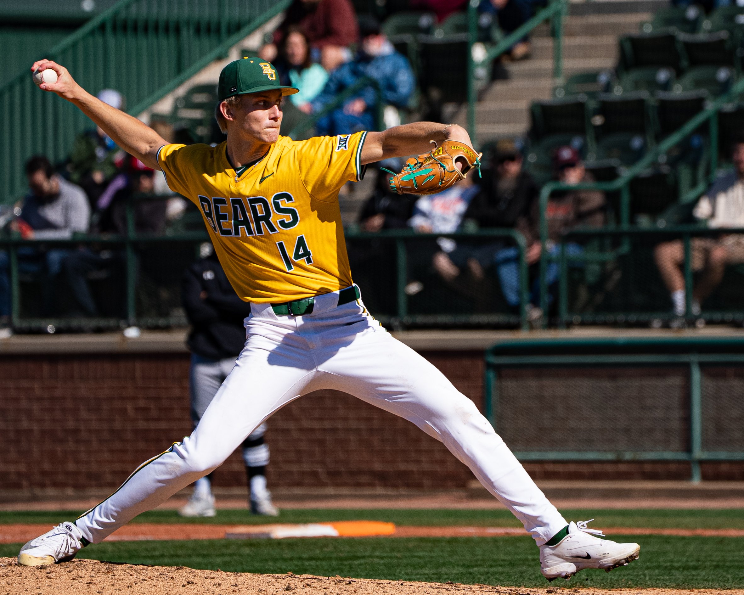 A baseball player in a green and yellow uniform preparing to throw a baseball on the field, with spectators in the background.