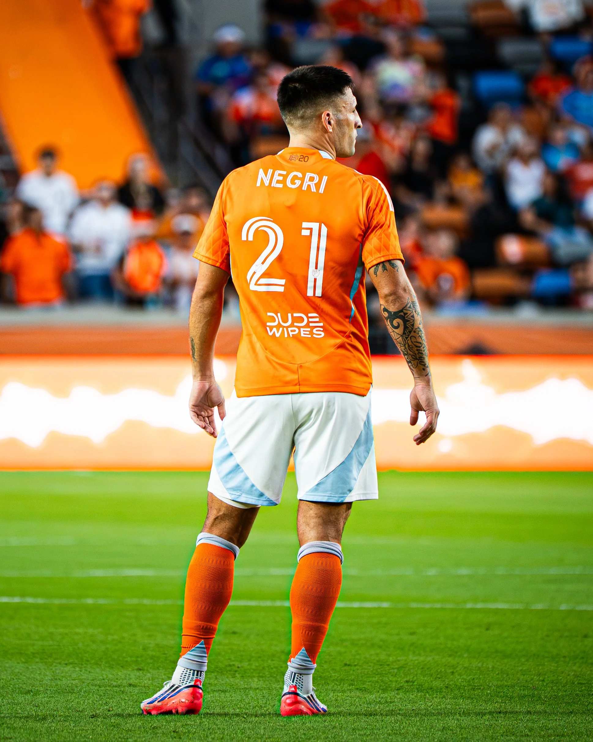 A soccer player in an orange jersey with the name 'Negrí' and the number 21, standing on a green field during a game, with a crowd of spectators in the background.