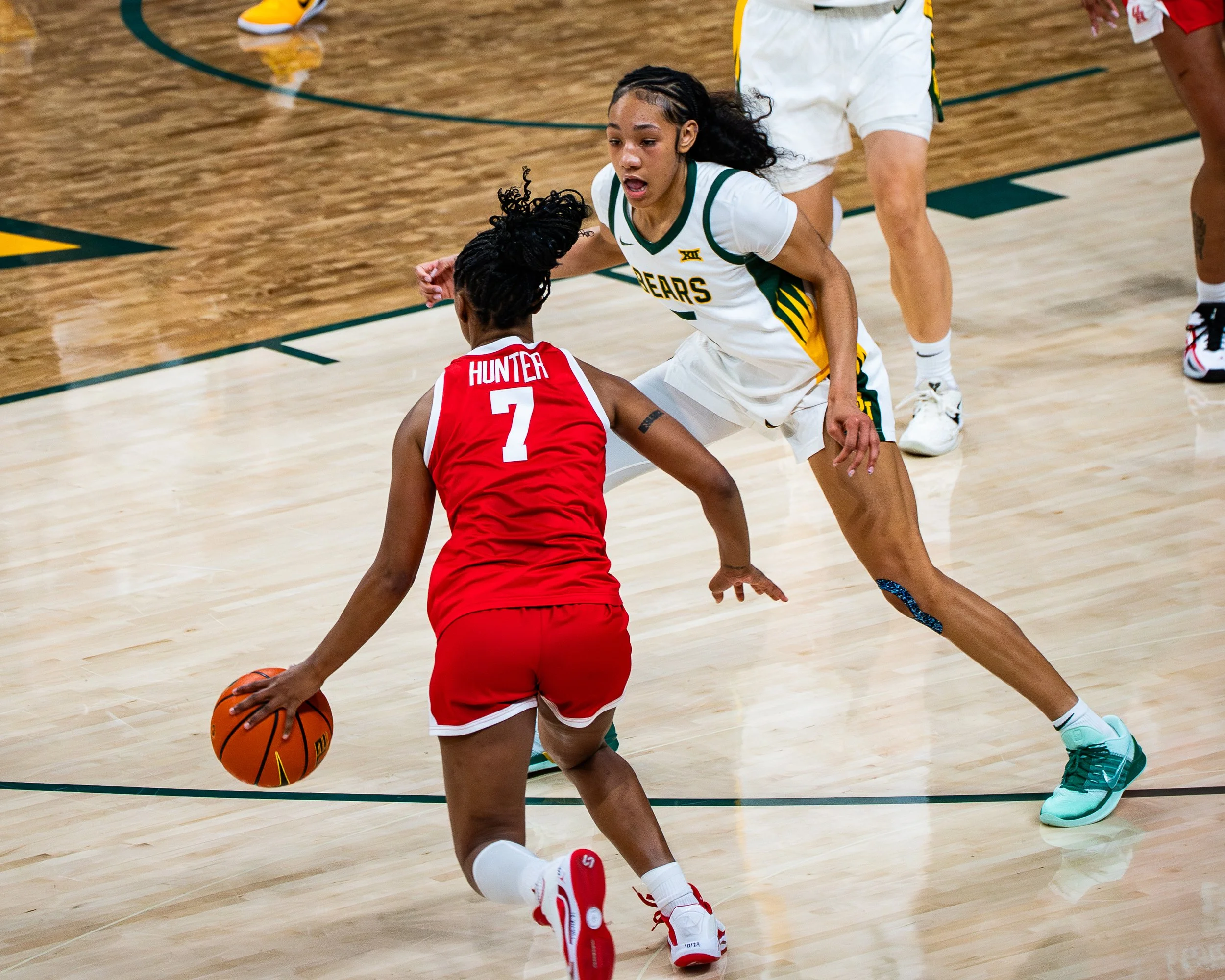 A women's basketball game in progress with two players close to the basket. One player wearing a green and white uniform with 