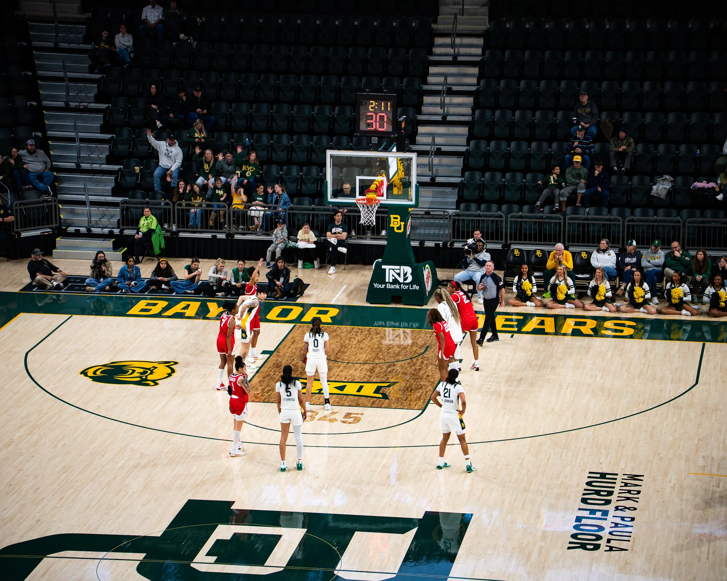 Basketball game at Baylor University with players on the court, cheerleaders on the sideline, and spectators seated in the stands.