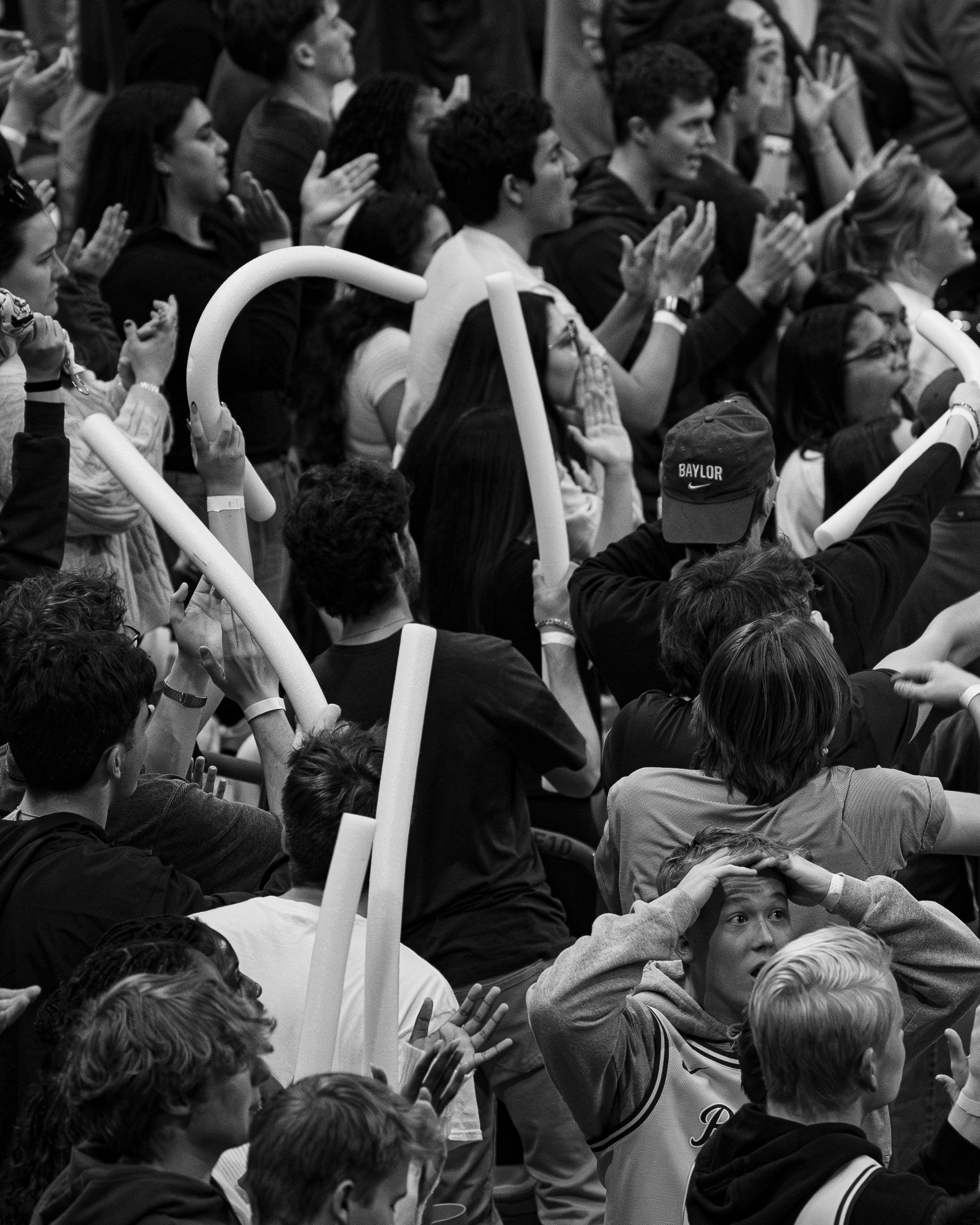 Black and white photograph of a gathering of diverse people, including children and adults, sitting close together. Some individuals are raising their hands, clapping, or attentively listening in what appears to be an indoor event or assembly.