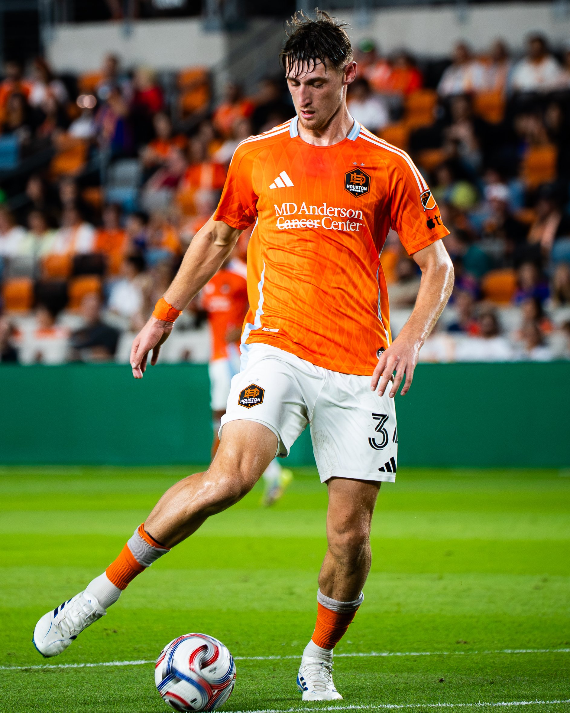 Soccer player in orange jersey controlling the ball on a field during a match.