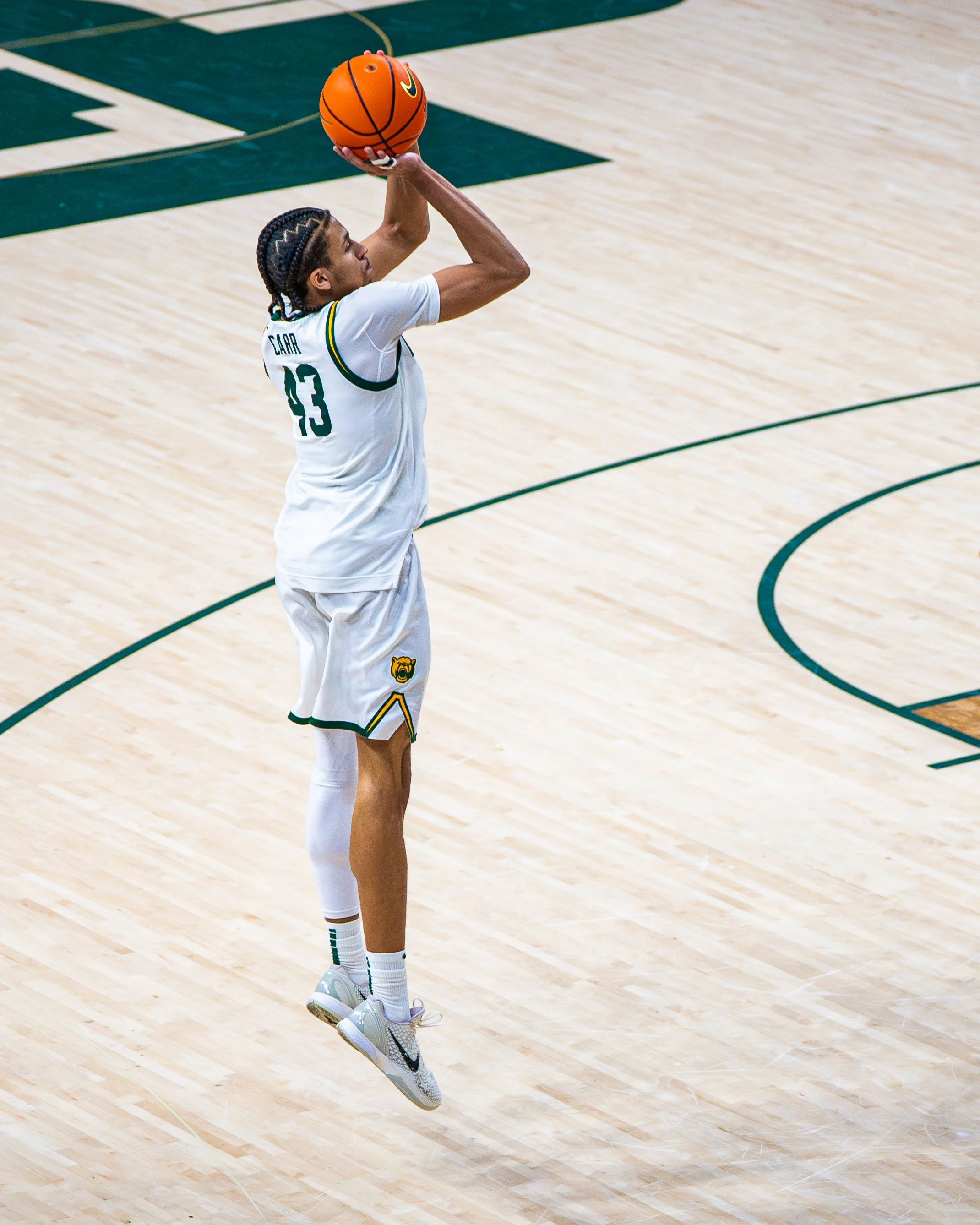 A basketball player in a white jersey with the number 13 and the name CARR, jumping to shoot a basketball on a basketball court.