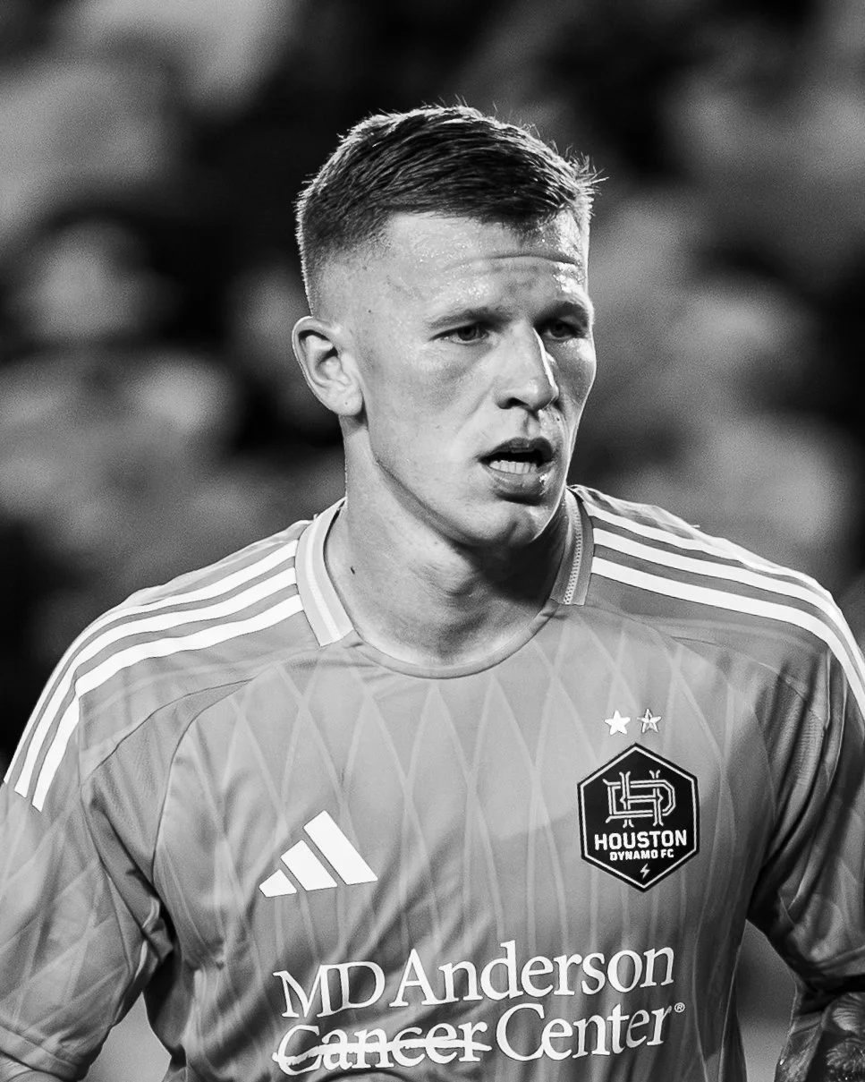 Black and white photo of a male soccer player wearing a Houston Dynamo FC jersey with sponsor MD Anderson Cancer Center logo, two stars above the club crest, and Adidas logo.