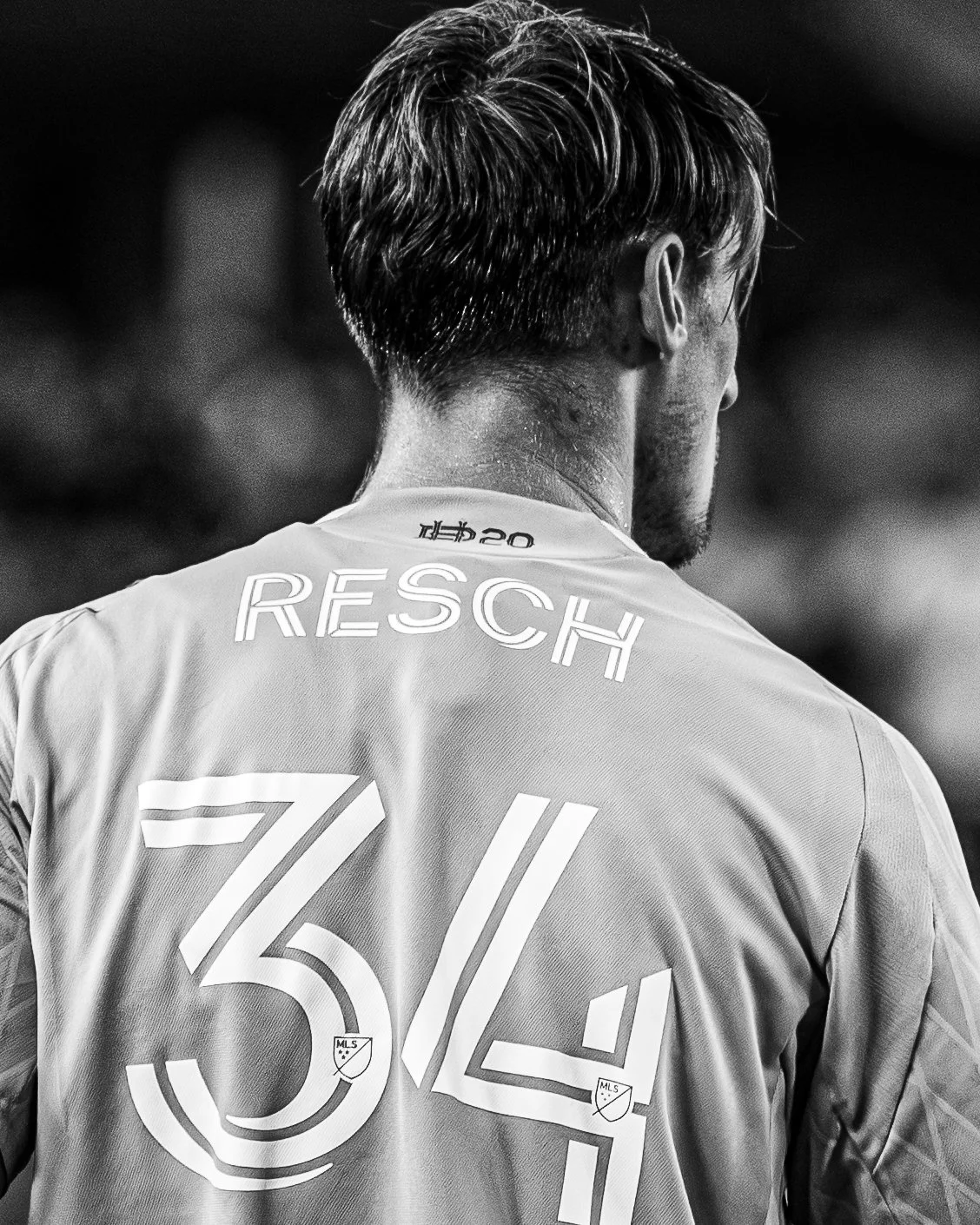 Black and white photograph of a male soccer player seen from behind, wearing a jersey with the name 'Resch' and the number '54'.