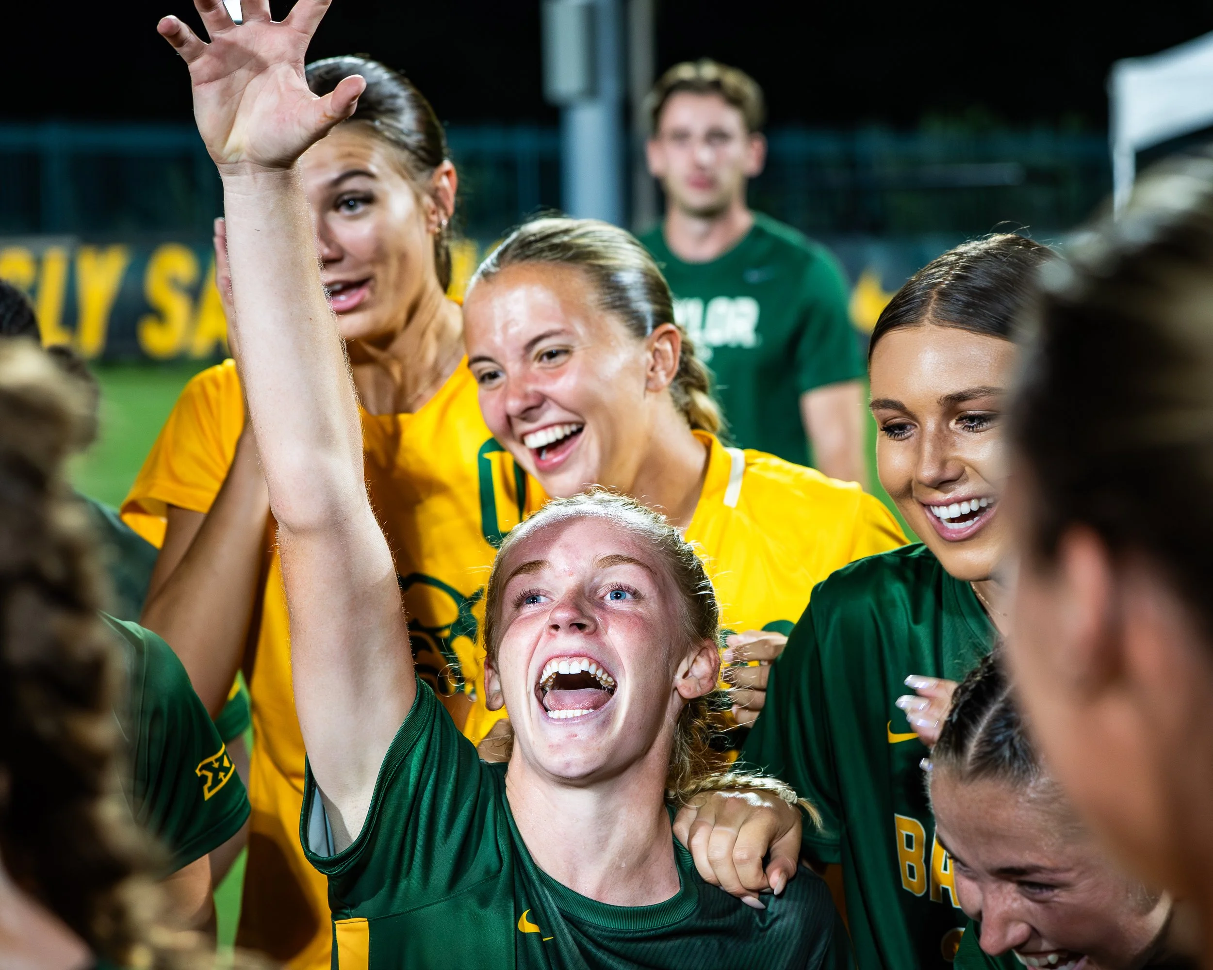 Group of female soccer players in green and yellow jerseys celebrating with high-fives and smiles.
